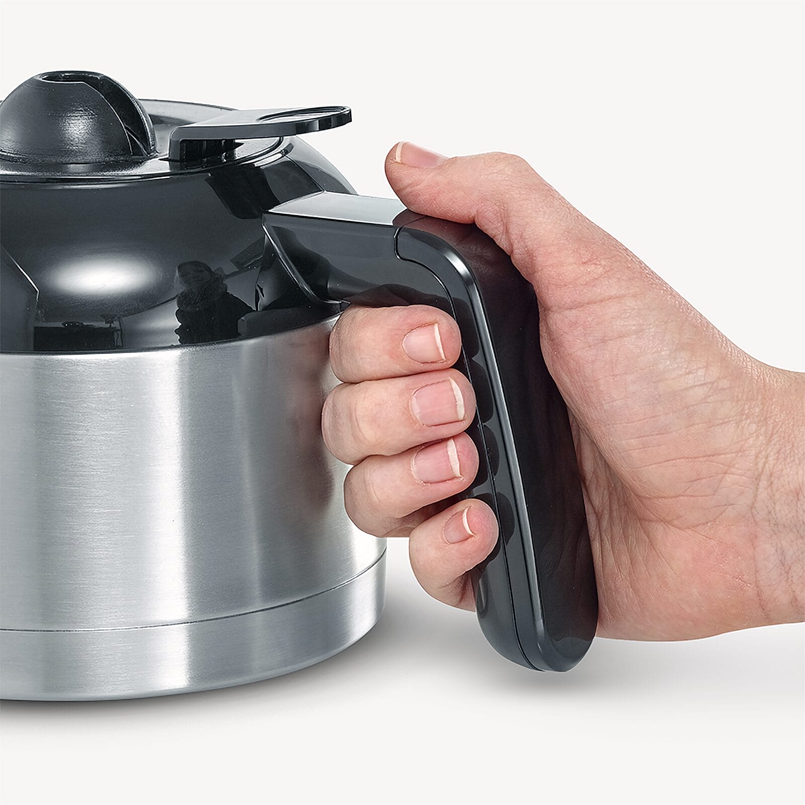 Dłoń chwyta czarną rączkę srebrnego czajnika.