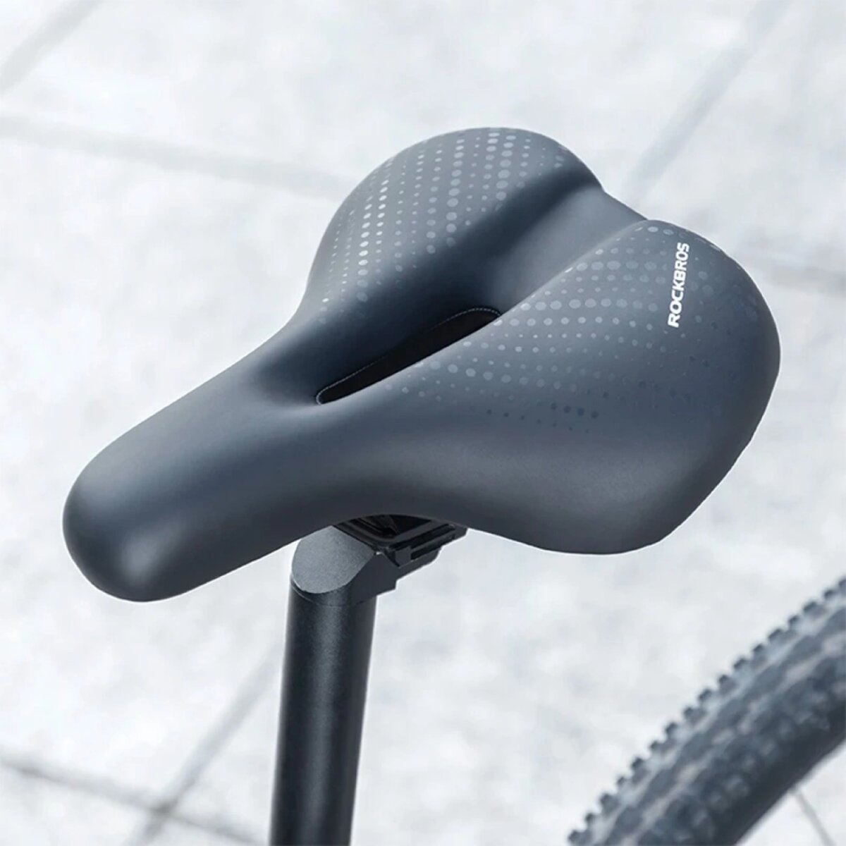 Schwarzer Fahrradsattel mit Punktmuster und Markenlogo, auf einem Pfosten montiert.