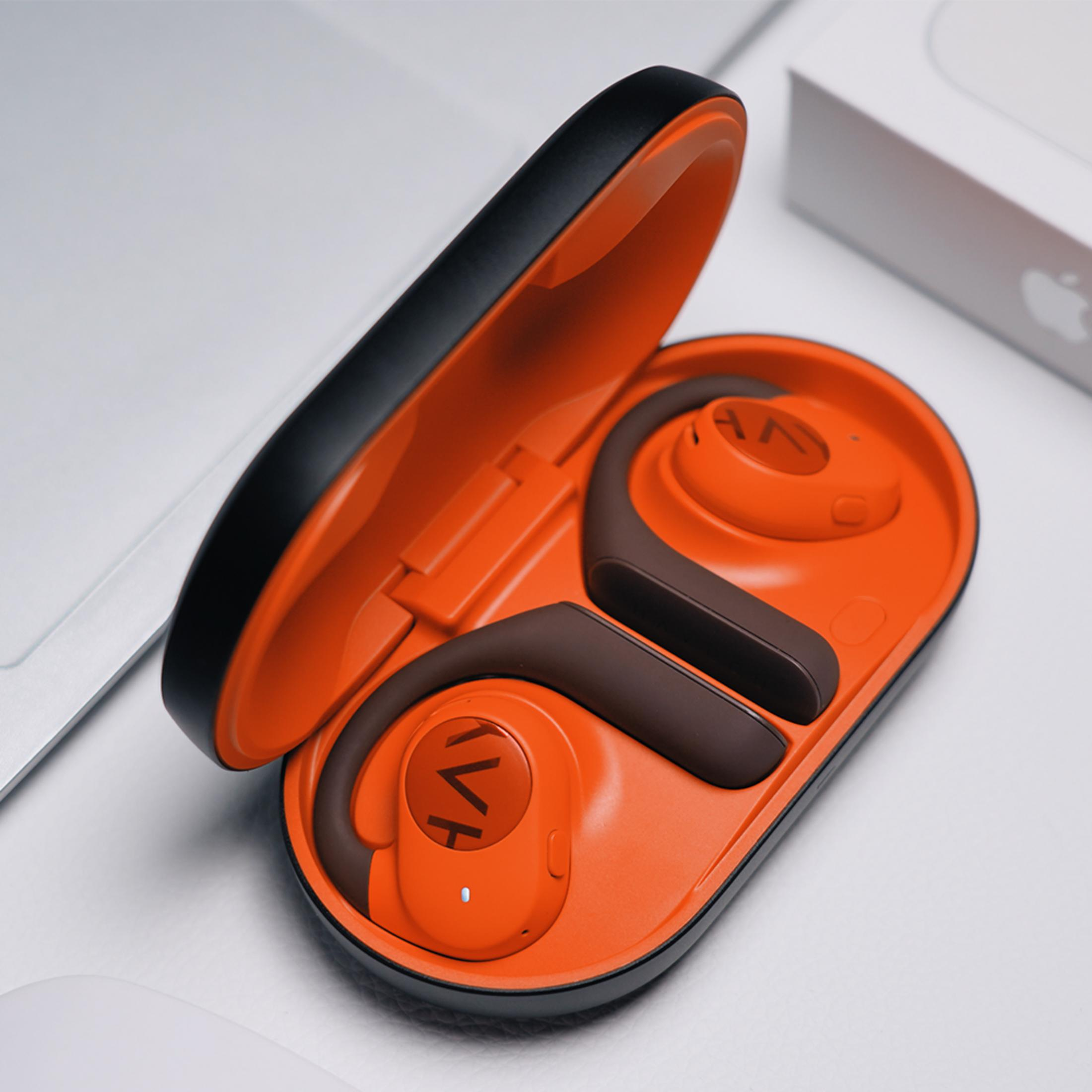 Orange und braune Ohrhörer in einer geöffneten Ladebox liegen auf einer weißen Oberfläche.