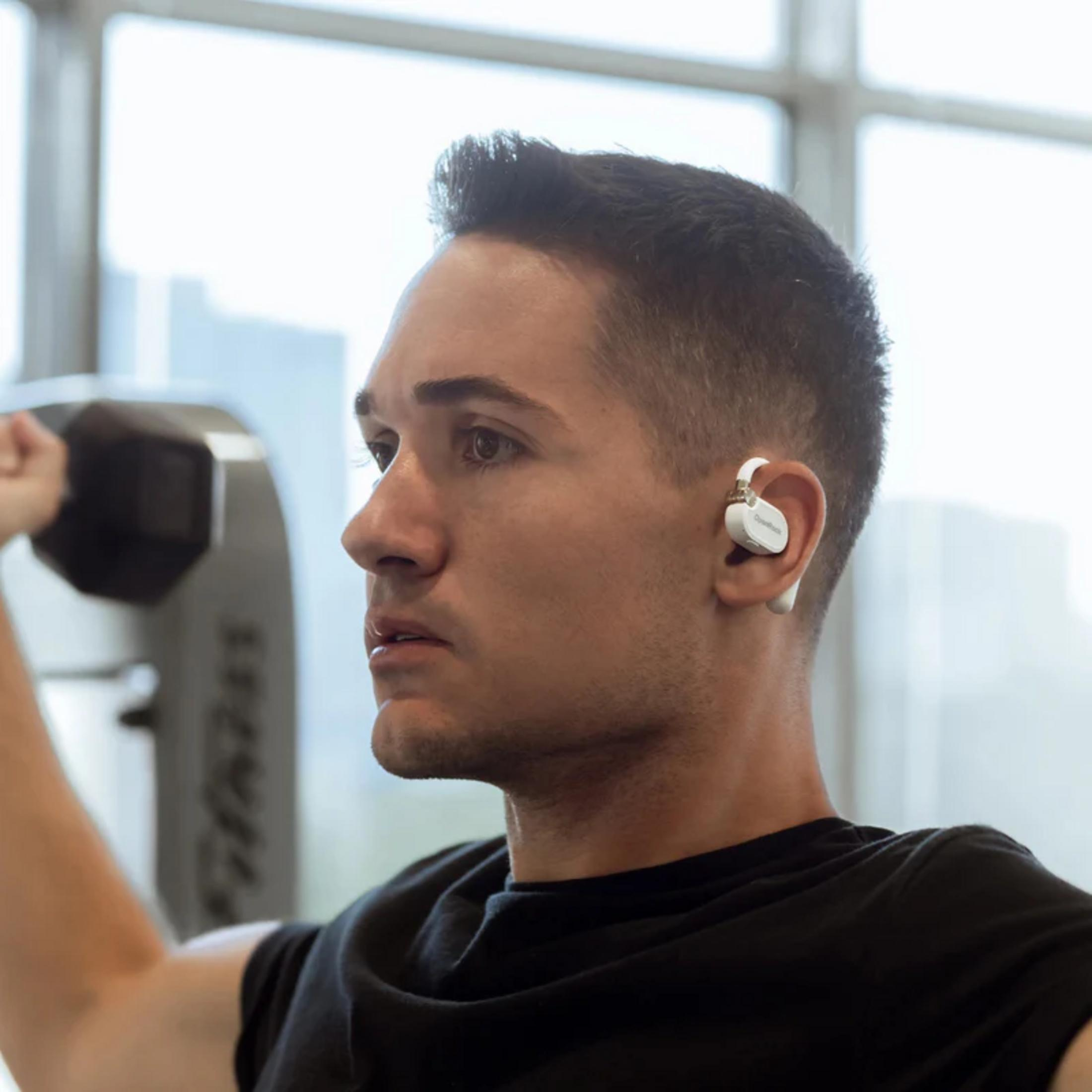 Man with white earbuds lifts dumbbell in gym. Focus on face and arm.