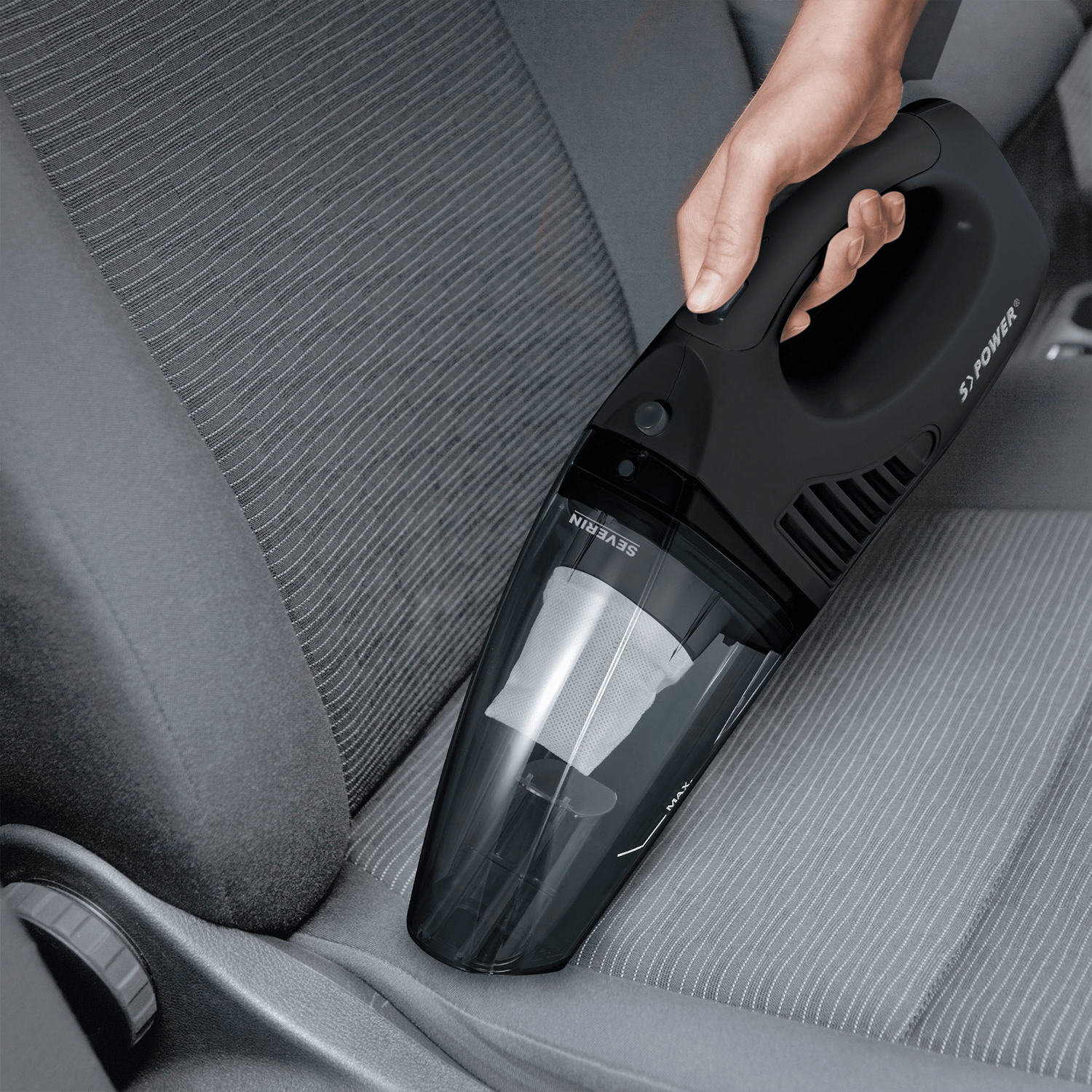 Mano tiene aspirapolvere portatile nero su sedile auto scuro.