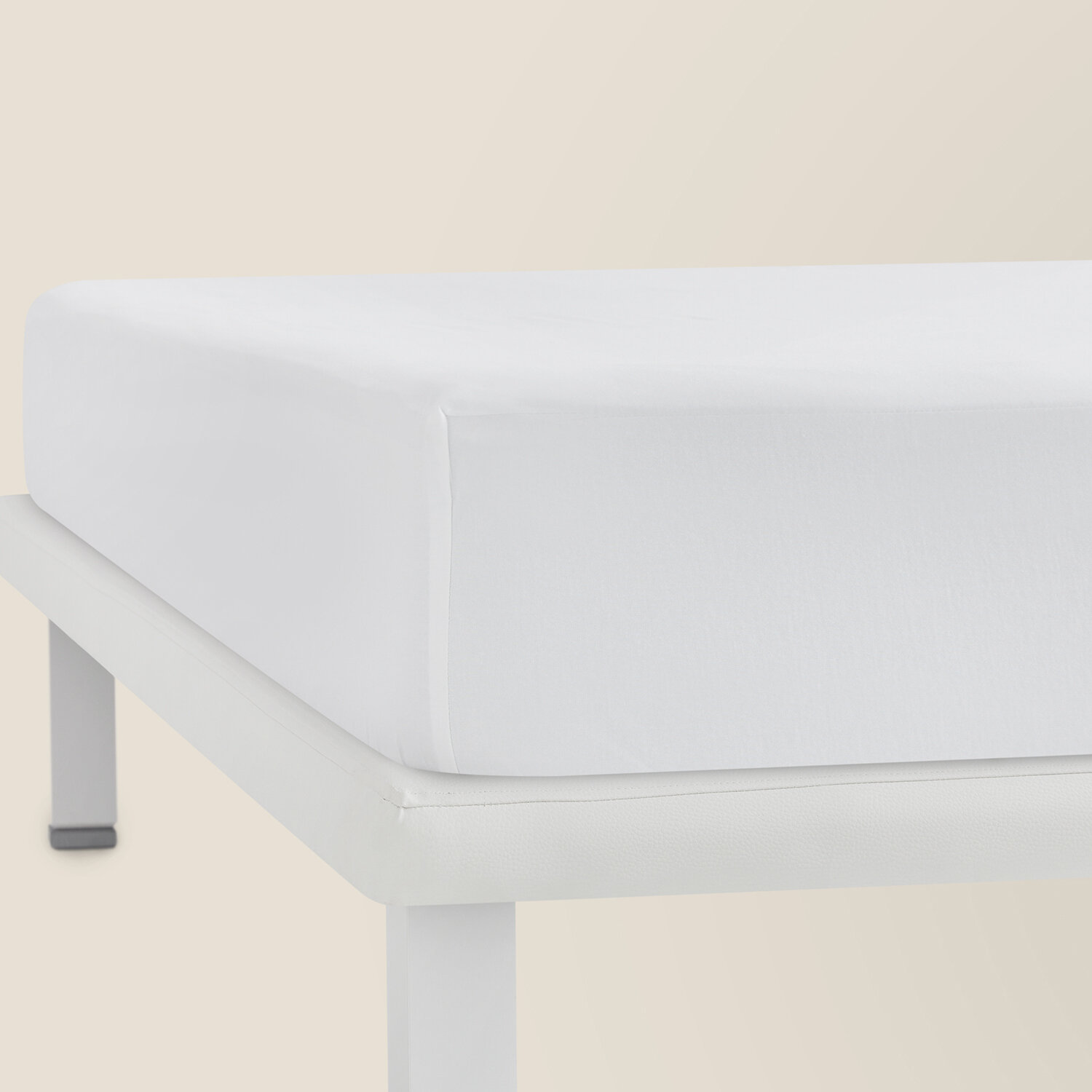 Una sábana bajera blanca sobre una estructura de cama blanca ante fondo claro.