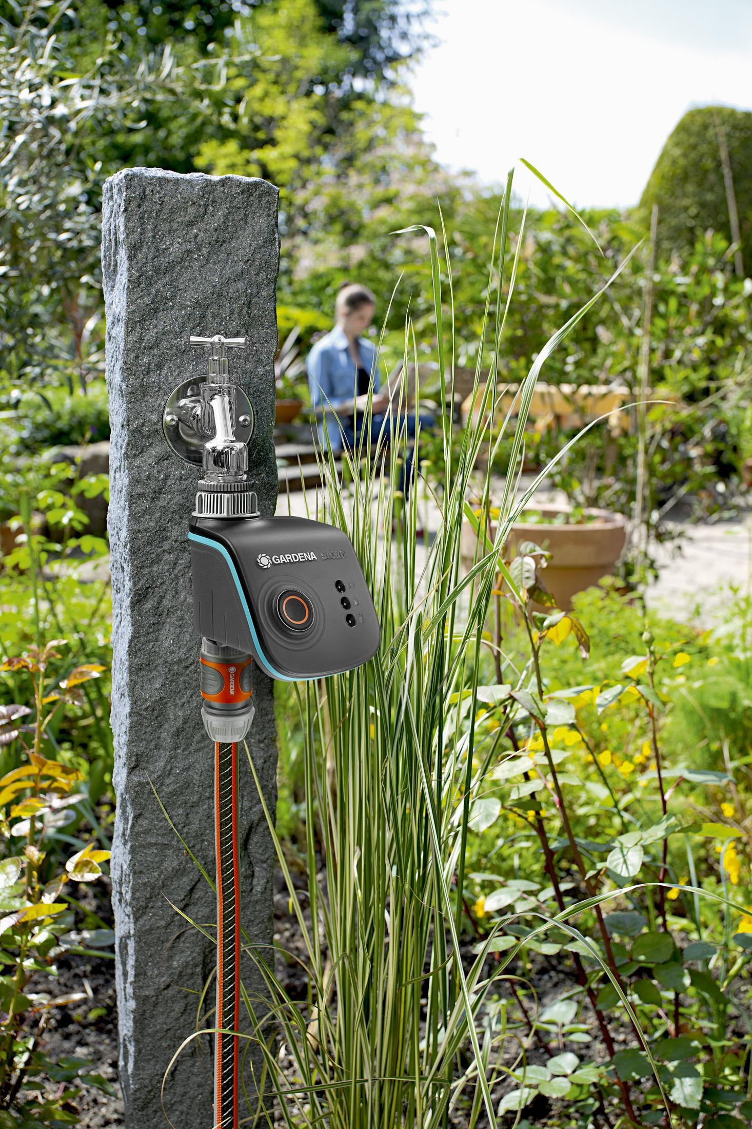 Un rubinetto da giardino con un programmatore di irrigazione su un palo di pietra.