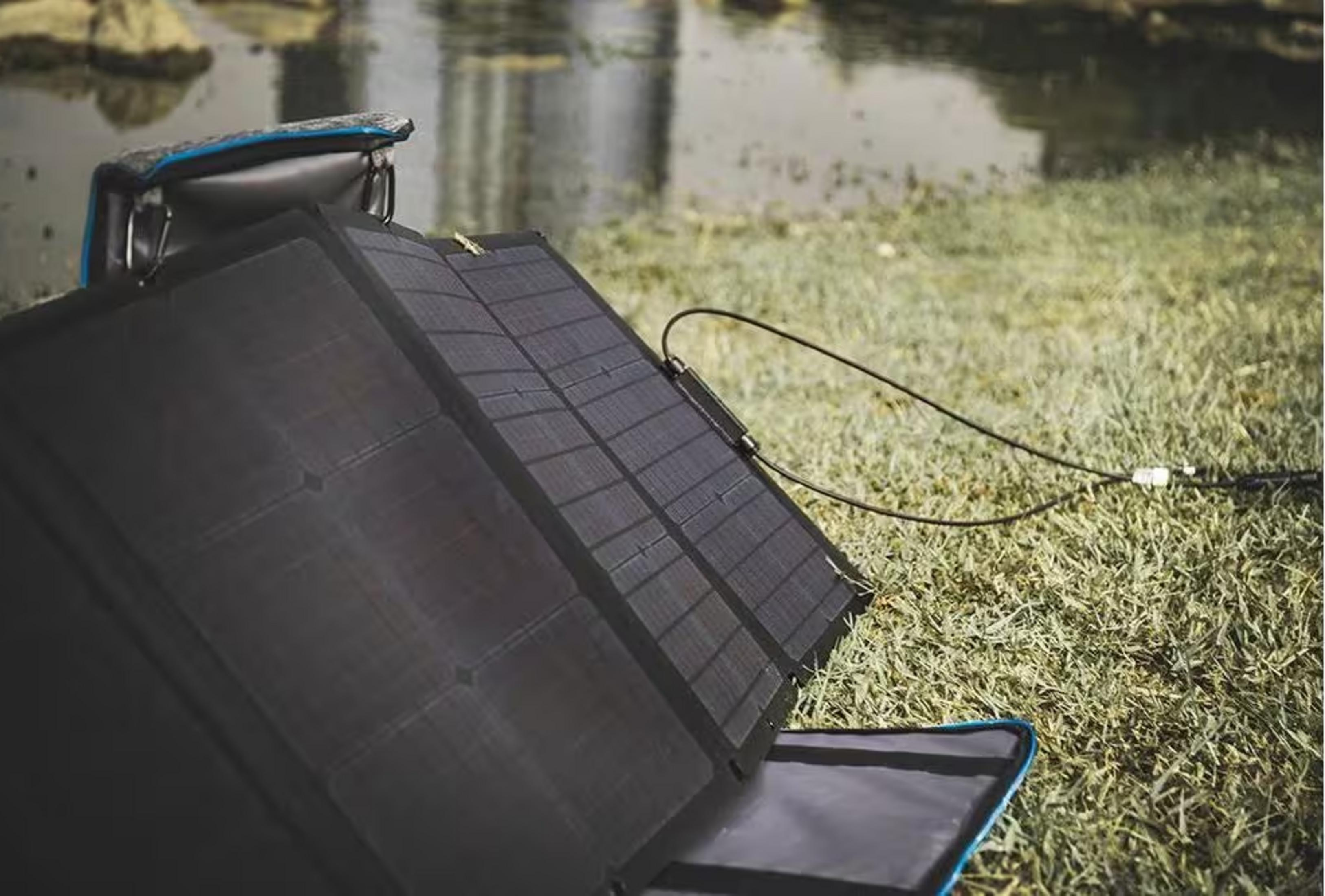 Składany panel słoneczny leży na trawie obok zbiornika wodnego.