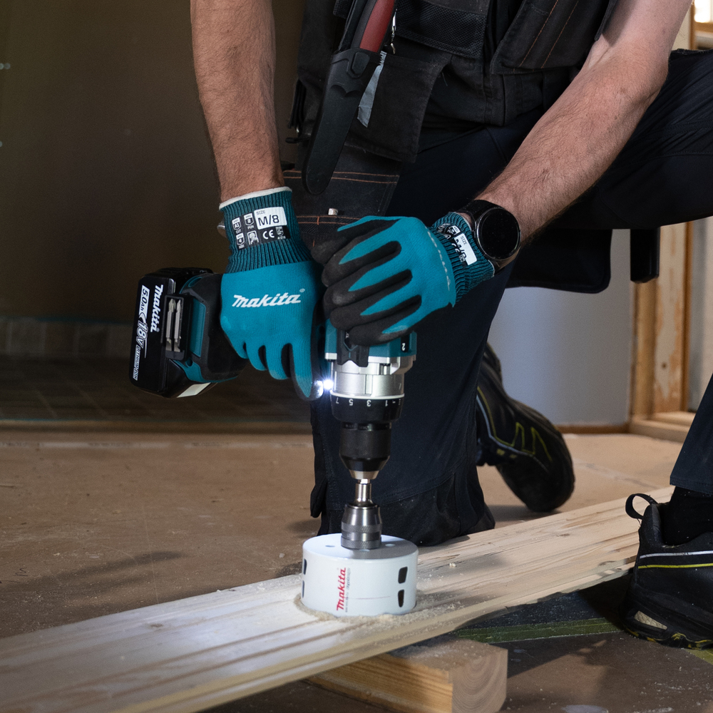 Operaio fora tavola di legno con segapunte bianco, indossa guanti blu.