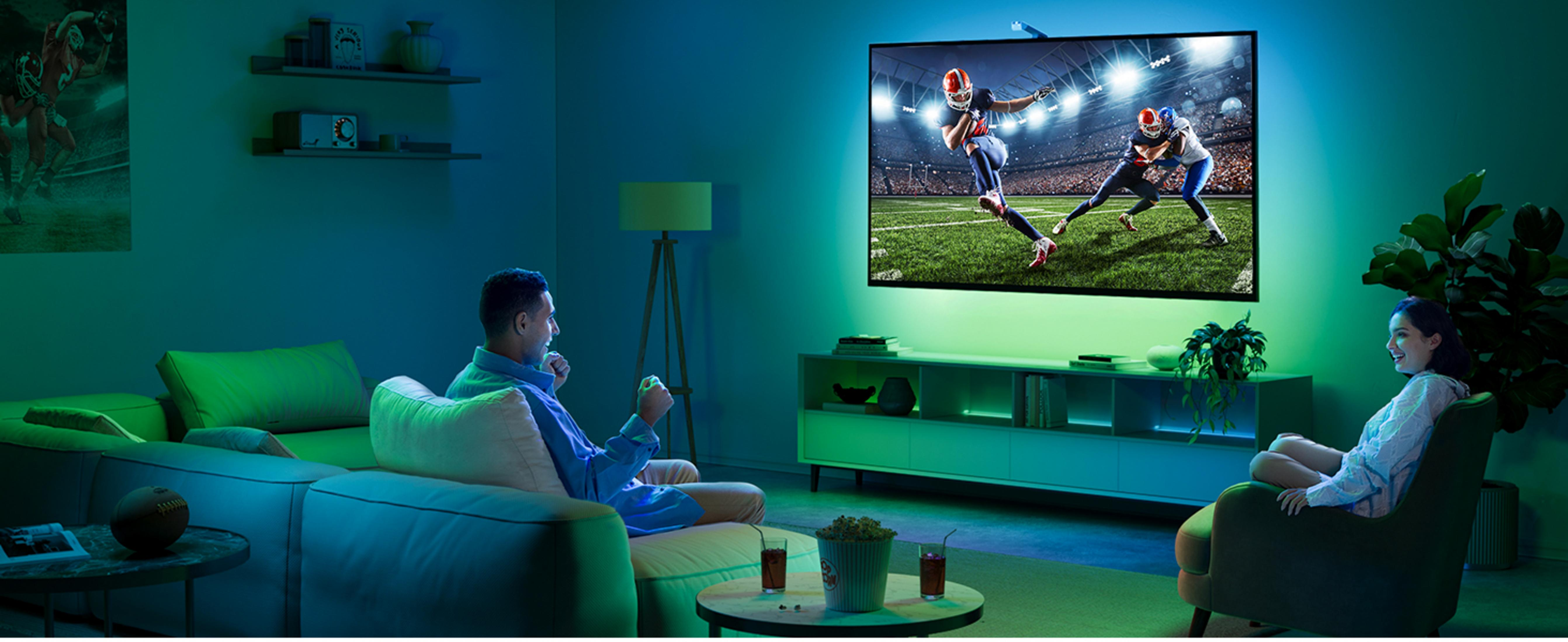 Mann und Frau sehen American Football im Wohnzimmer mit Umgebungsbeleuchtung.