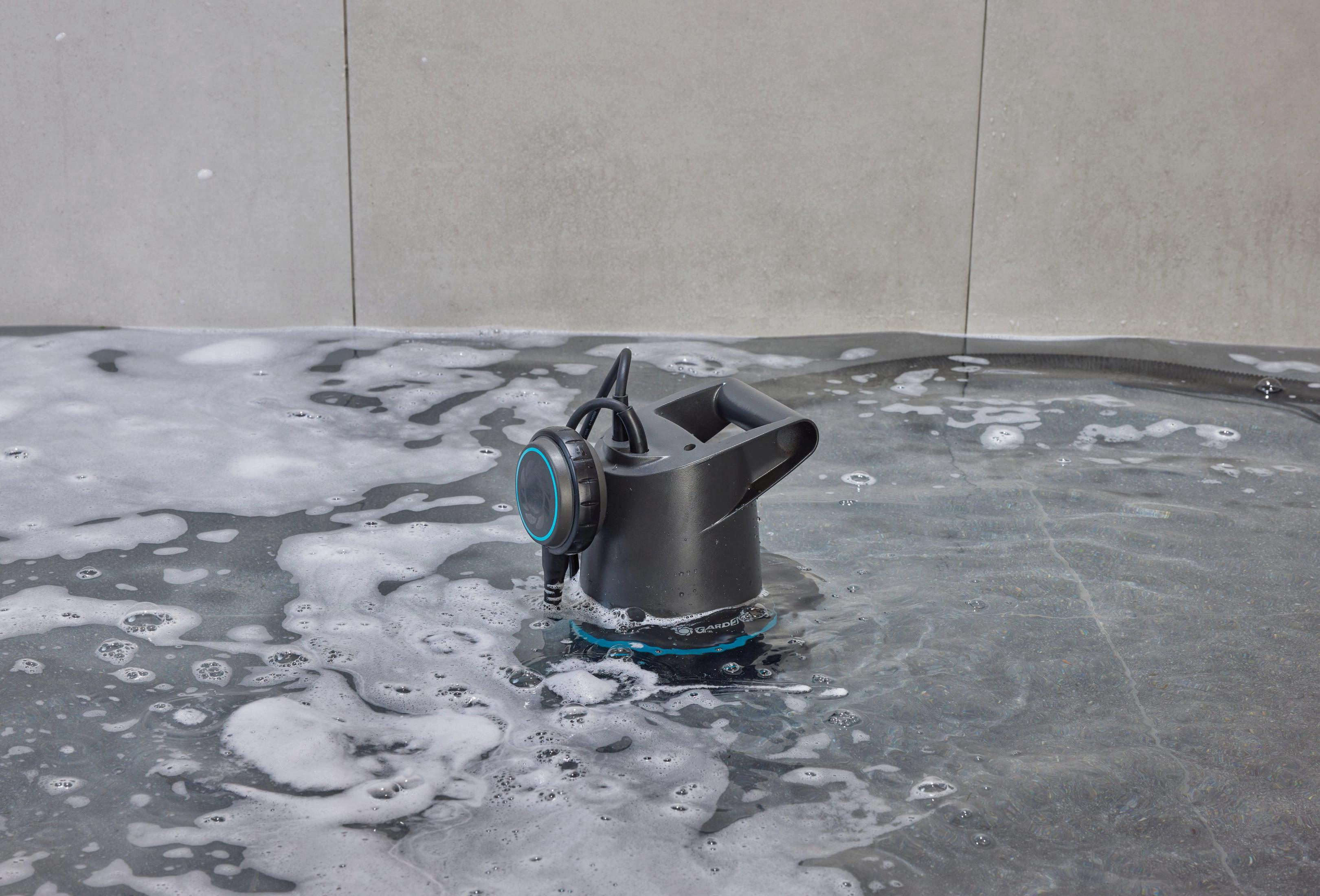 Czarny czajnik z pompą zanurzeniową stoi w spienionej wodzie na szarej podłodze.