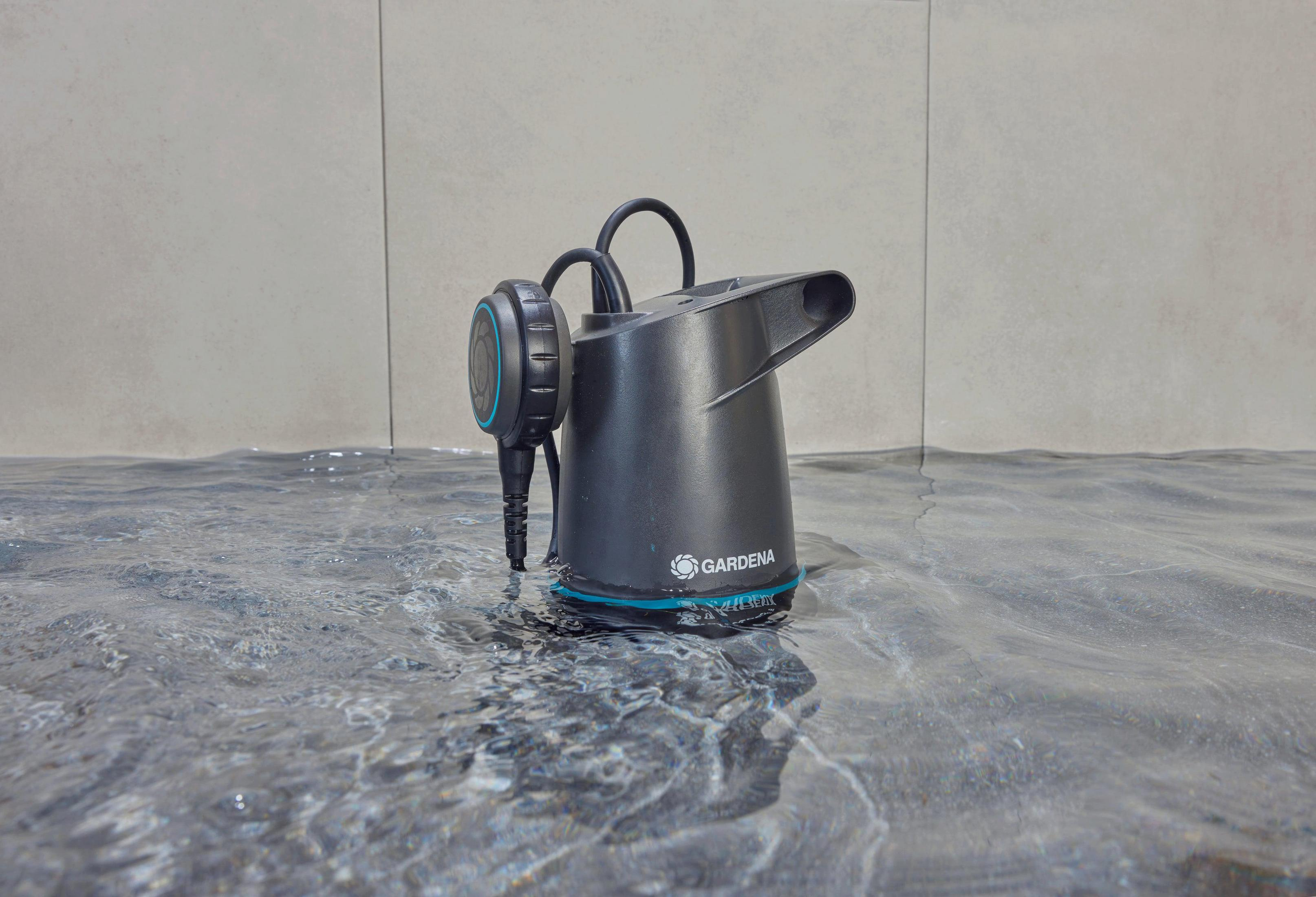 Czarna pompa zanurzeniowa z logo Gardena w wodzie na szarym, kafelkowym tle.