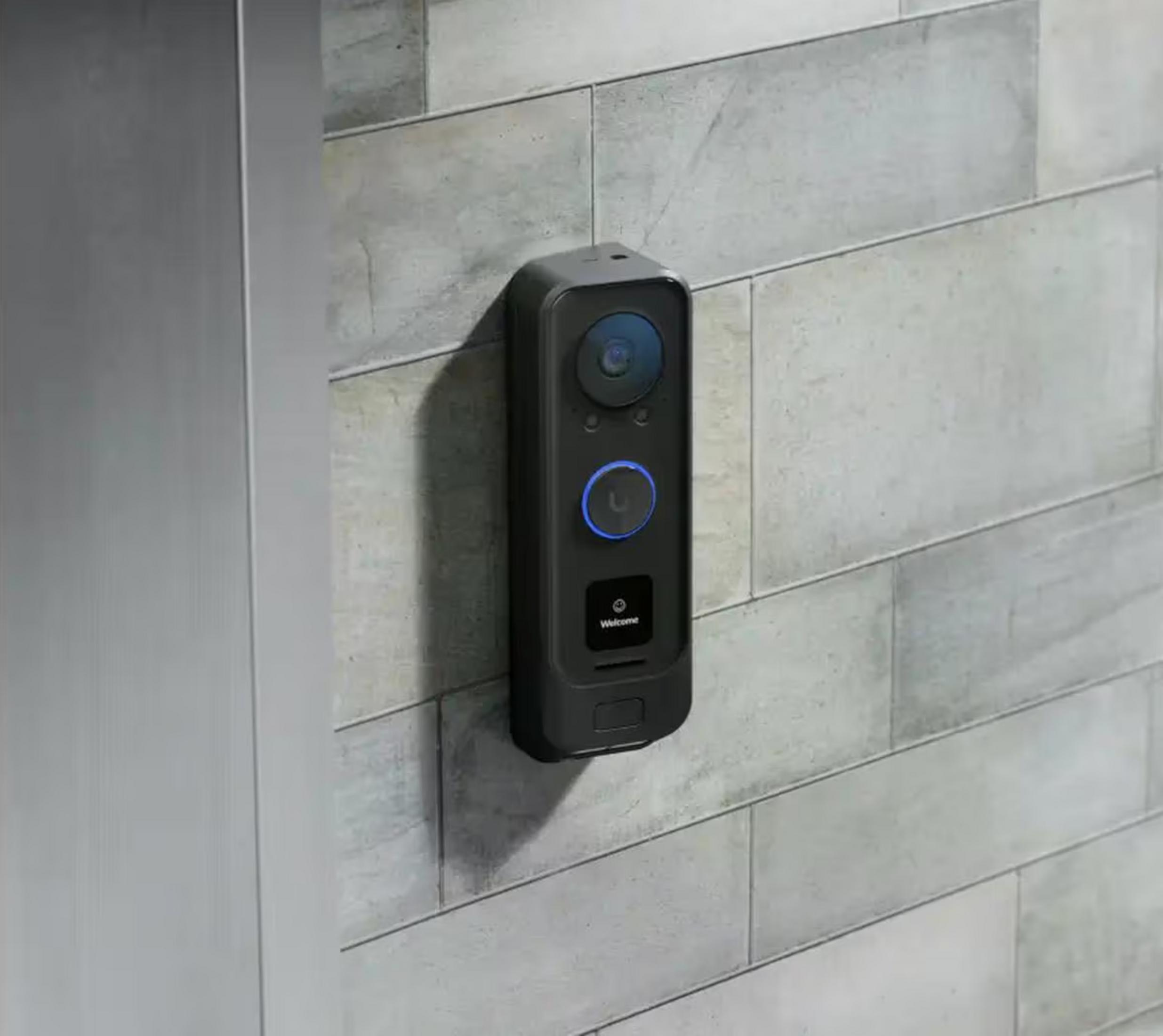 A black doorbell camera with a blue light ring on a grey tiled wall.