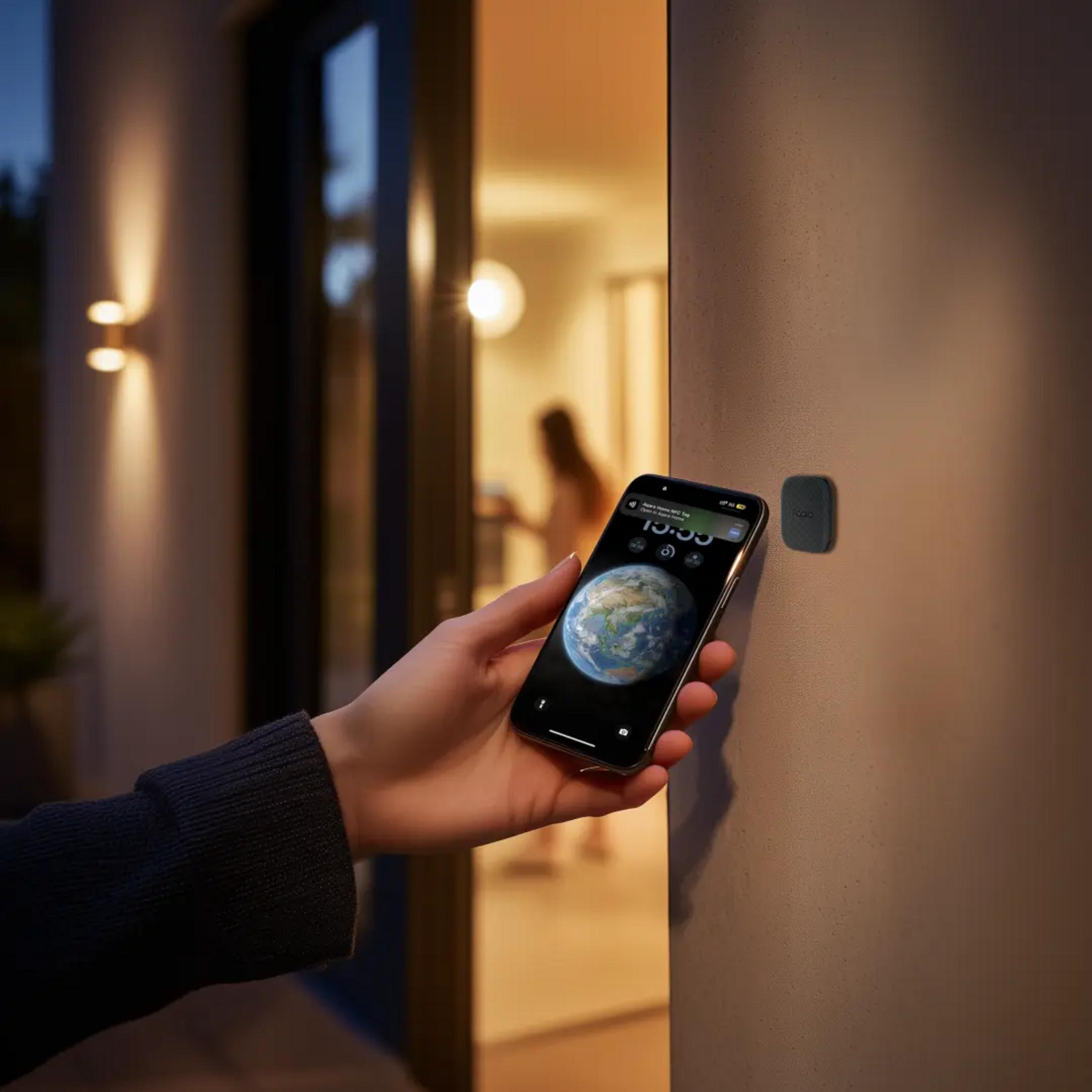 Eine Hand hält ein Smartphone mit Erd-Wallpaper vor einer Hauswand mit einem NFC-Tag.