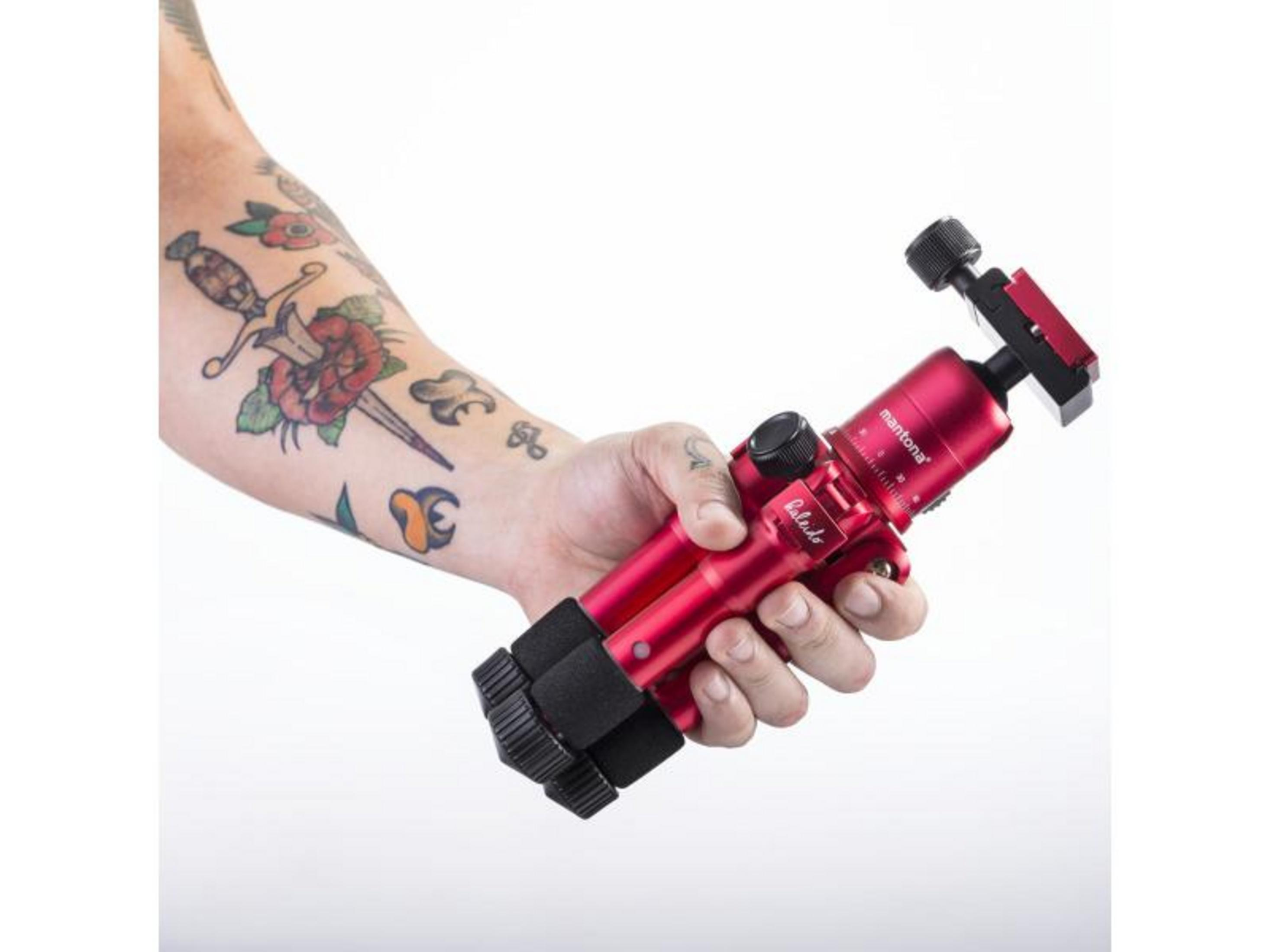 Ramię z tatuażem trzyma czerwony statyw Mantona z czarnymi uchwytami.
