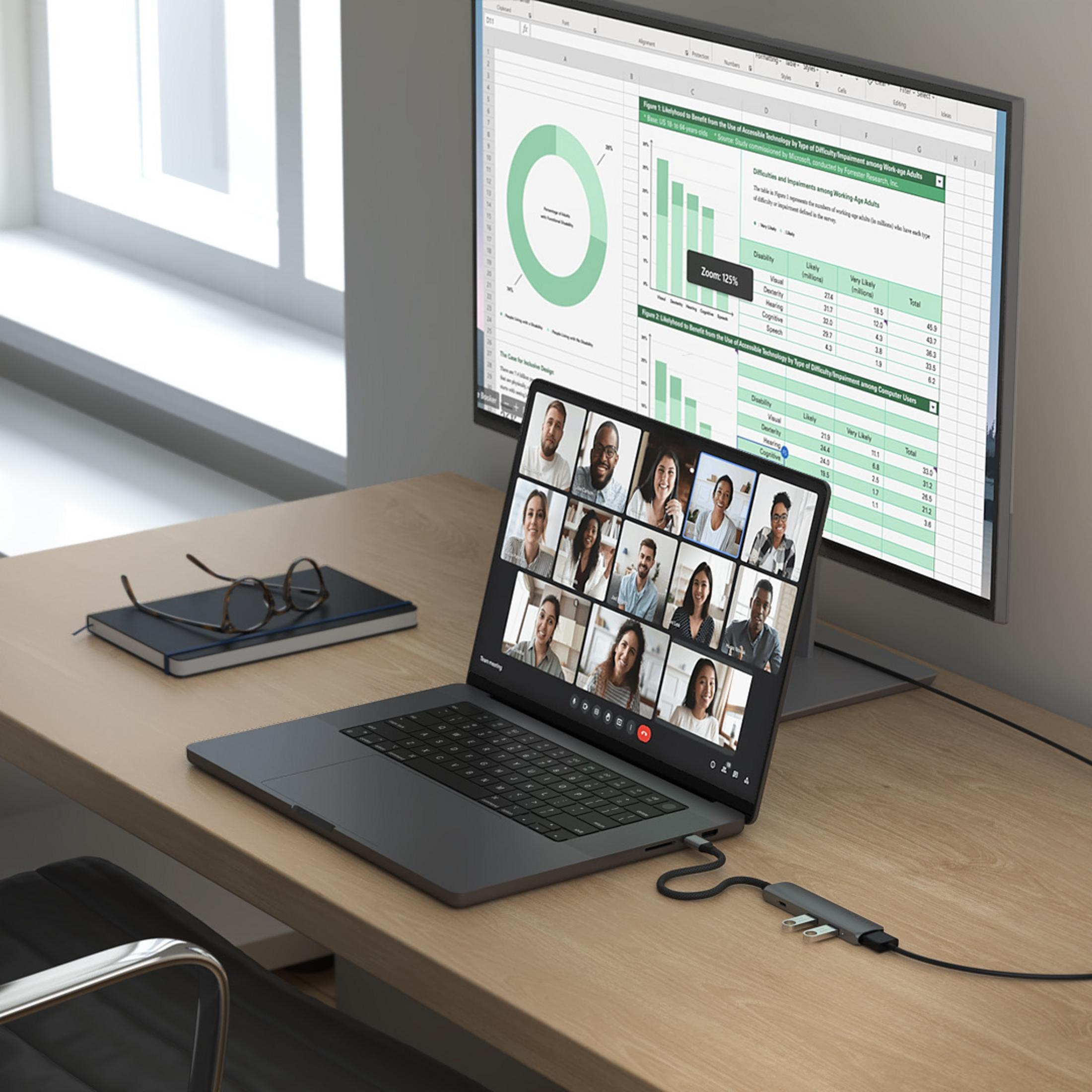 Ein Laptop zeigt eine Videokonferenz mit vielen Personen, ein externer Monitor zeigt Diagramme.