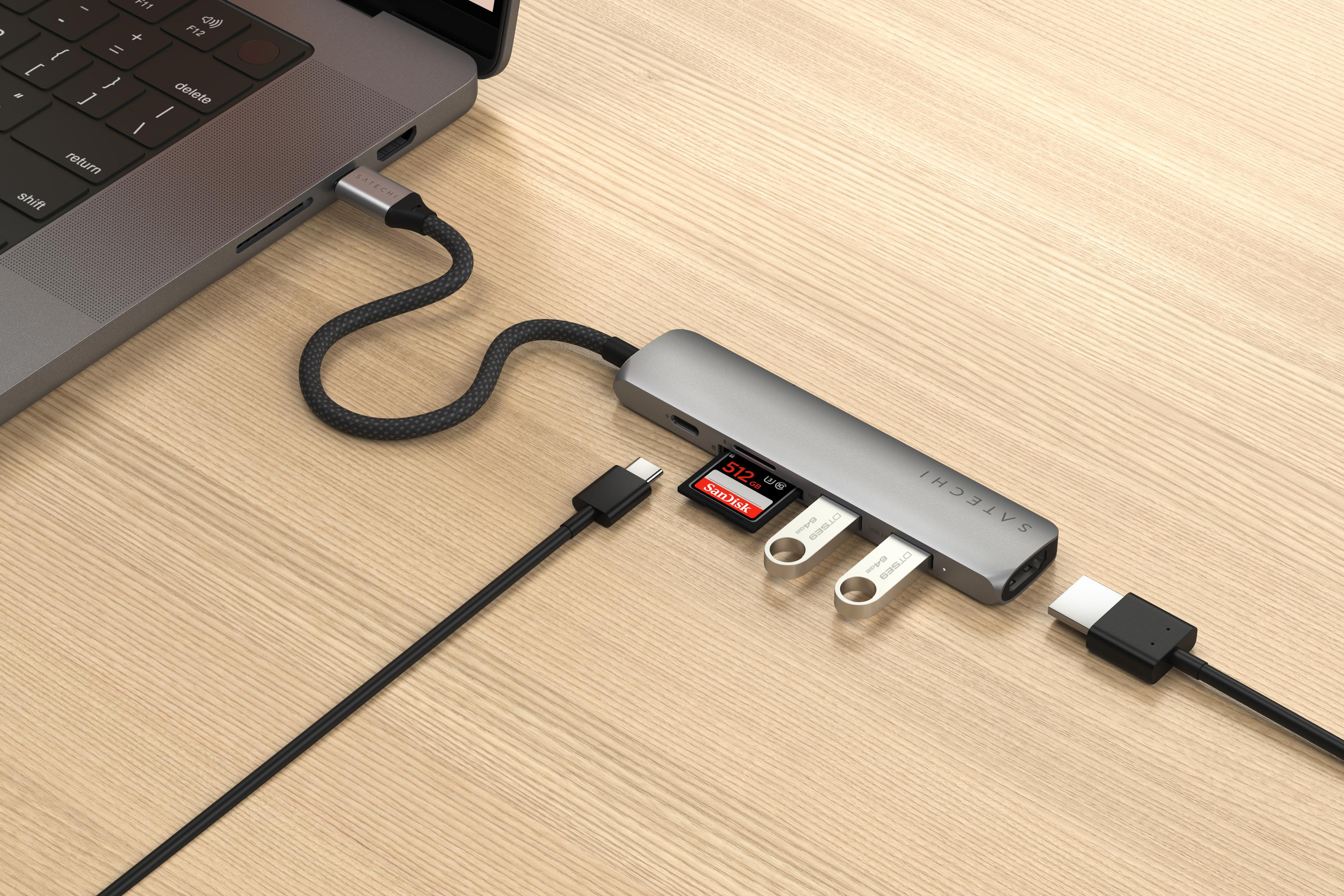 Ein grauer USB-C-Hub mit SD-Karte, zwei USB-Sticks und Kabeln an einem Laptop.