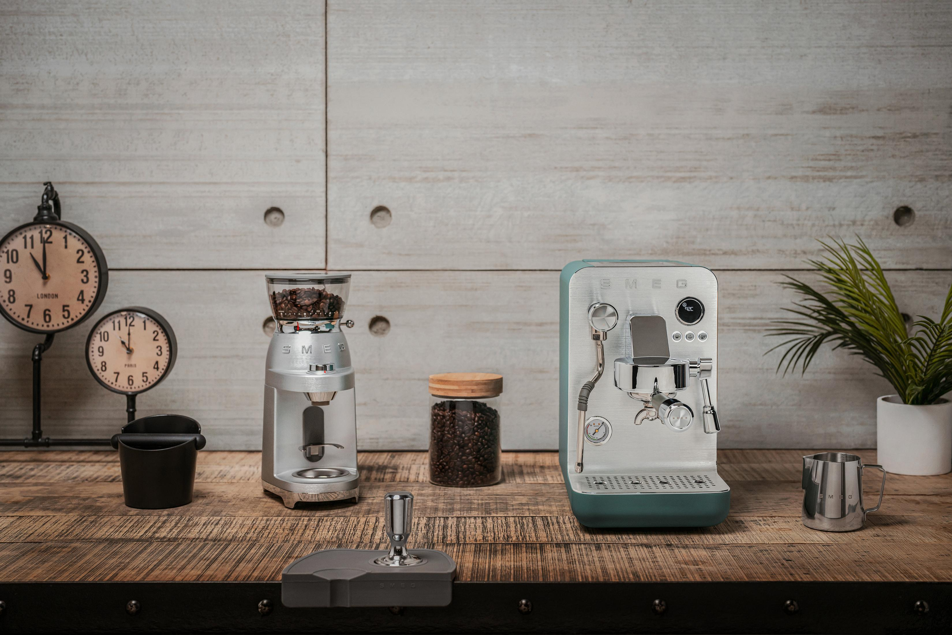 Máquina de espresso, molinillo, granos, tazas y relojes en mesa madera.