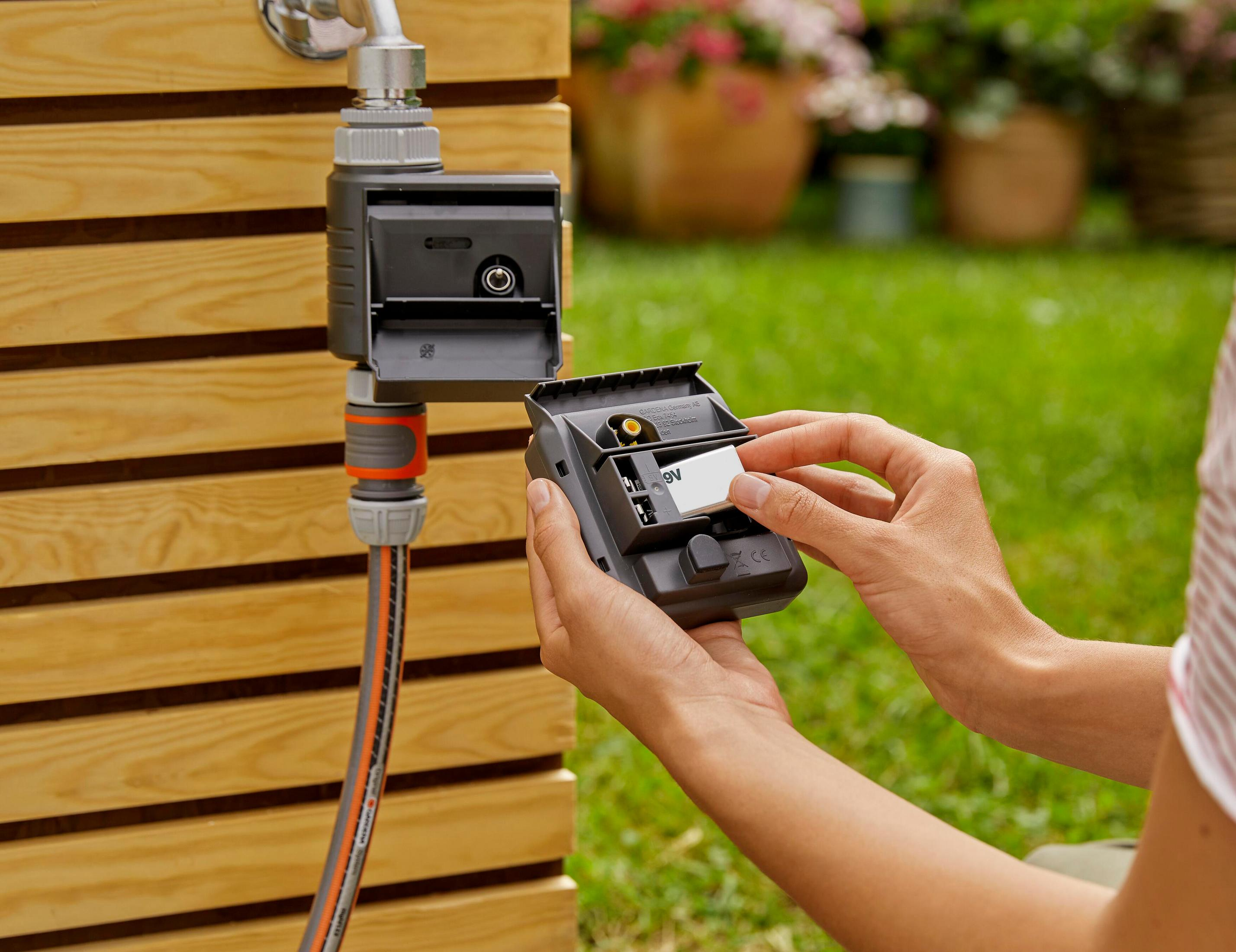 Person setzt 9V Batterie in schwarzen Gartenschlauch-Timer ein.
