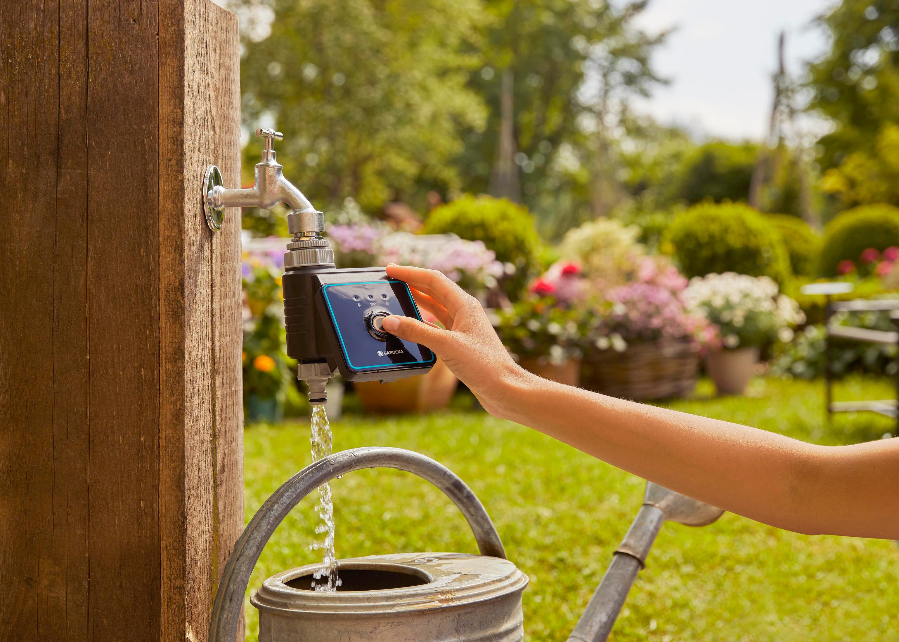 Eine Hand bedient einen Wasserhahn-Timer, während Wasser in eine Gießkanne fließt.