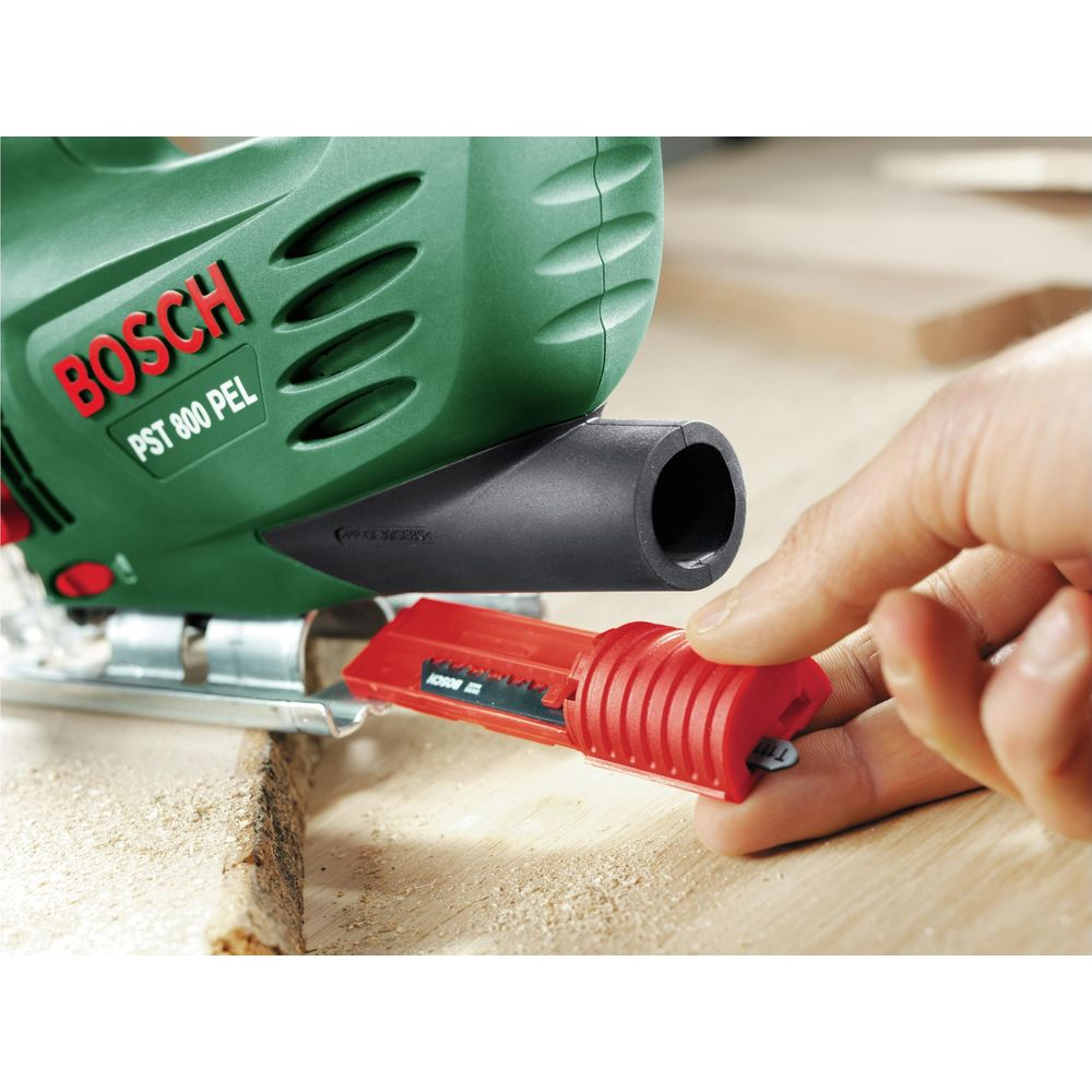 Ręka trzyma czerwony element do zielonej wyrzynarki Bosch na drewnie.
