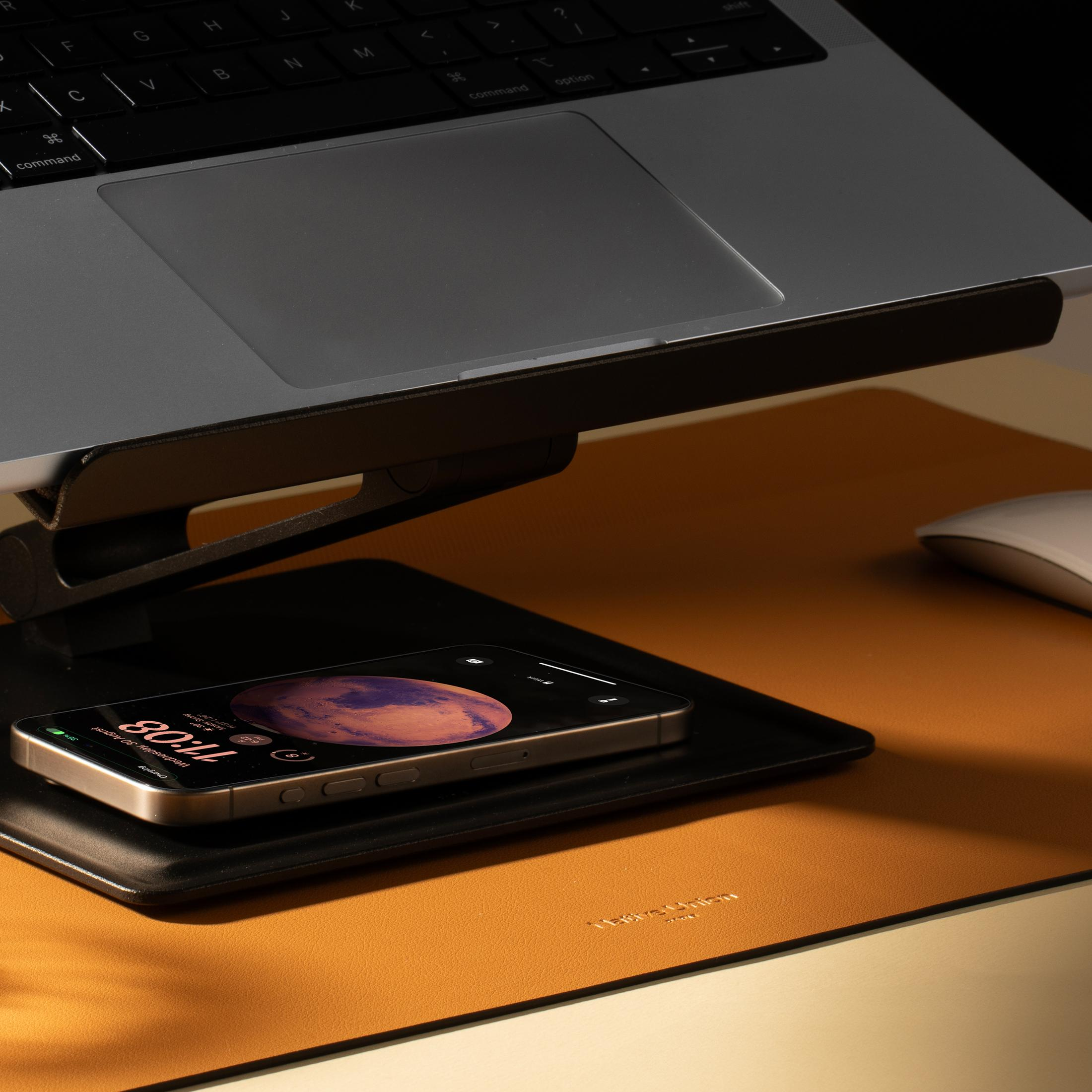 Un laptop è sopra un telefono in carica su un tappetino in pelle.