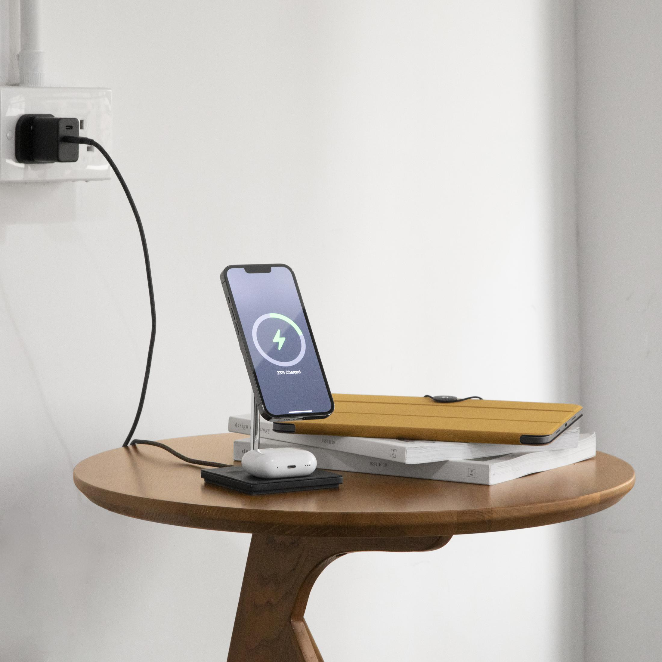 Un telefono si carica su un supporto, accanto a auricolari e una custodia gialla per tablet su libri.