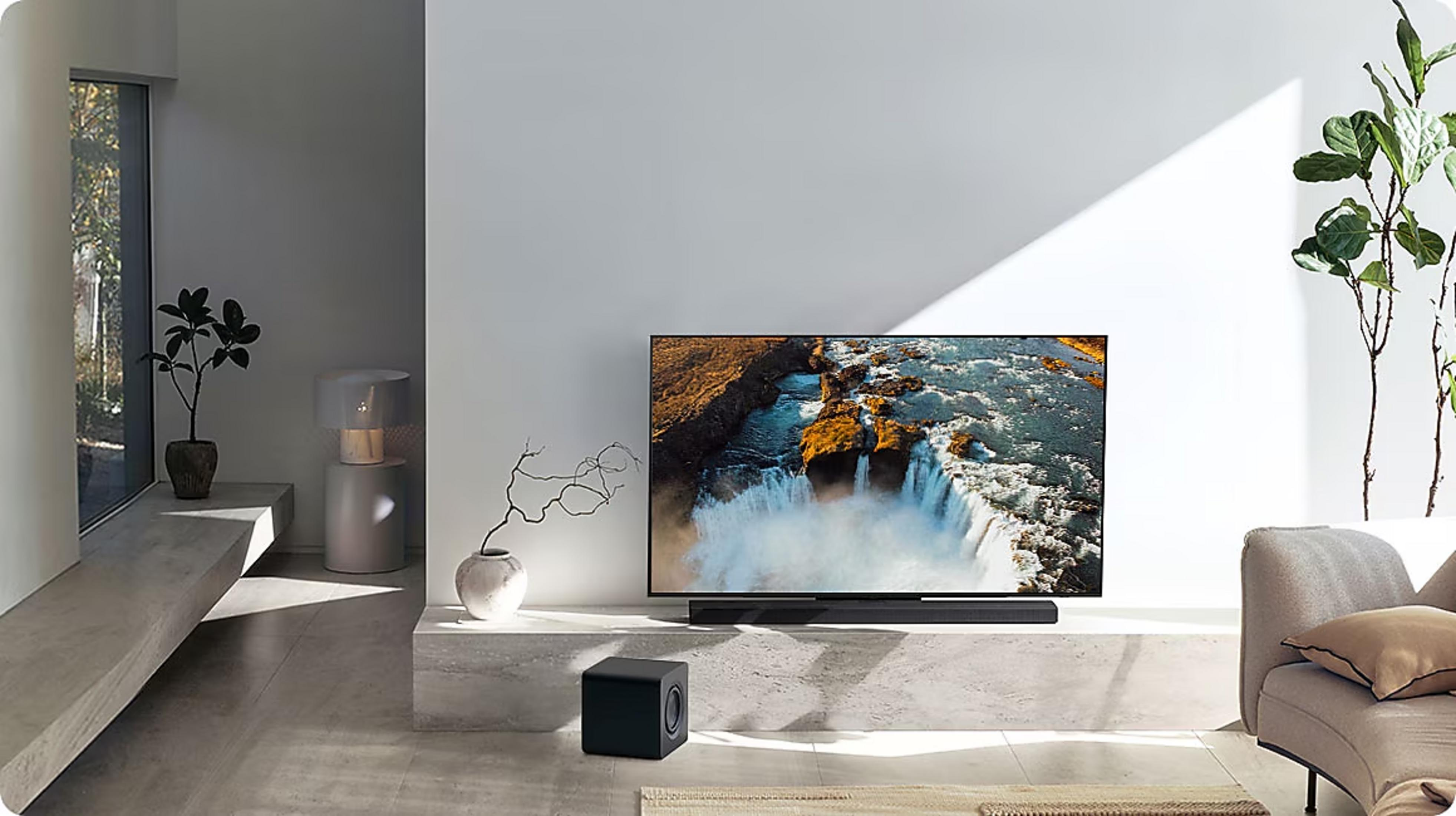 Salon moderne avec TV montrant une cascade, barre de son, caisson de basses et plante.