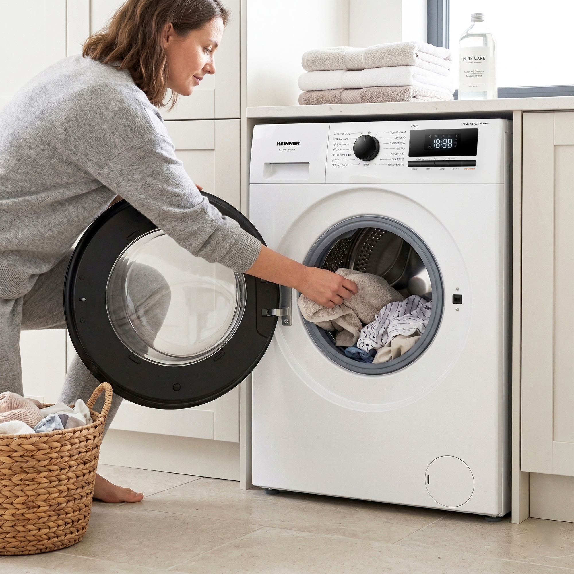 Eine Frau lädt Wäsche in eine weiße Waschmaschine. Ein Wäschekorb steht daneben.