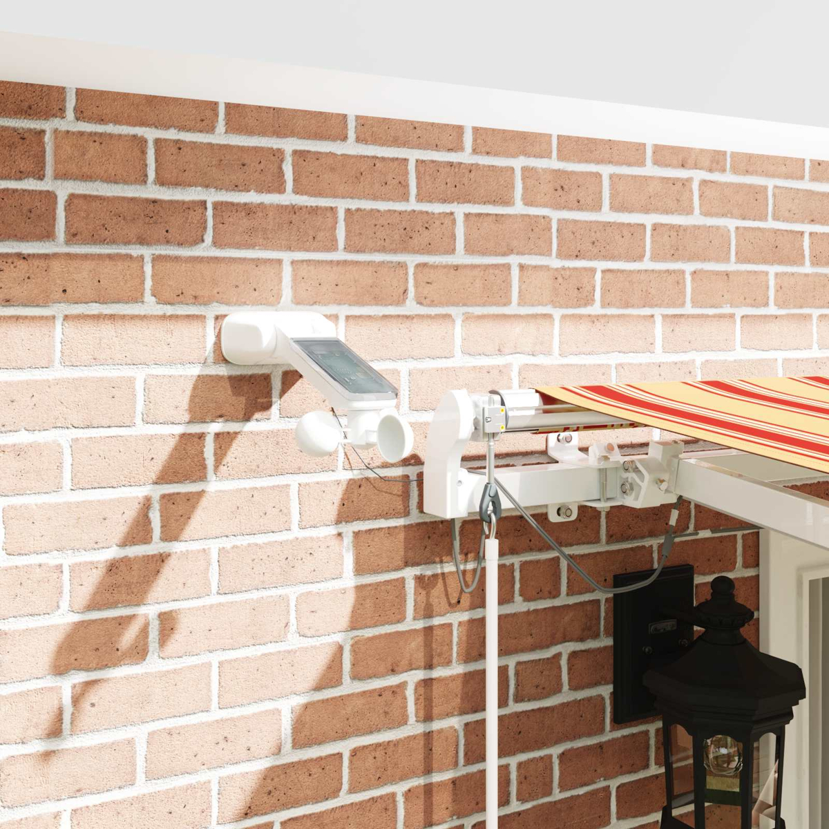 Weißes Wettergerät mit Solarpanel an Ziegelwand neben Markise und Laterne.