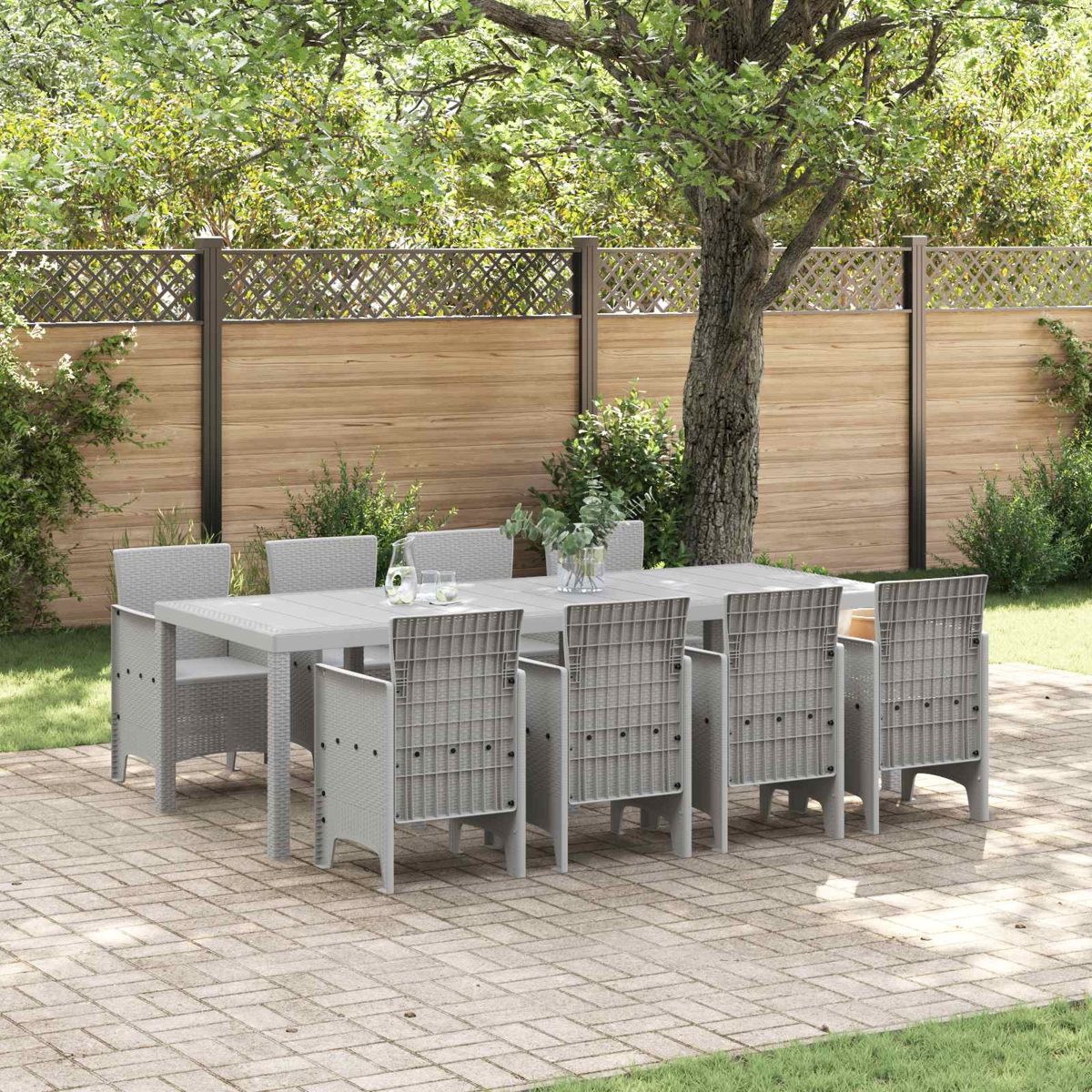 Grauer Tisch und acht Stühle im Freien auf einer Terrasse mit Holzzaun und Bäumen.