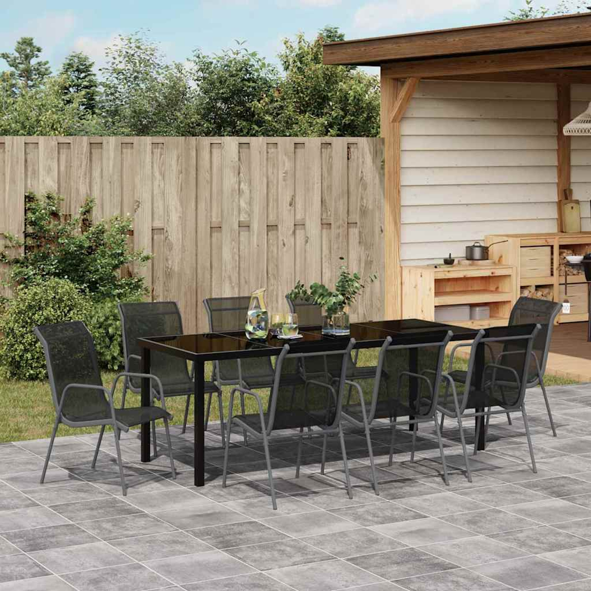 Conjunto de comedor exterior con mesa y sillas negras en patio alicatado, junto a valla.