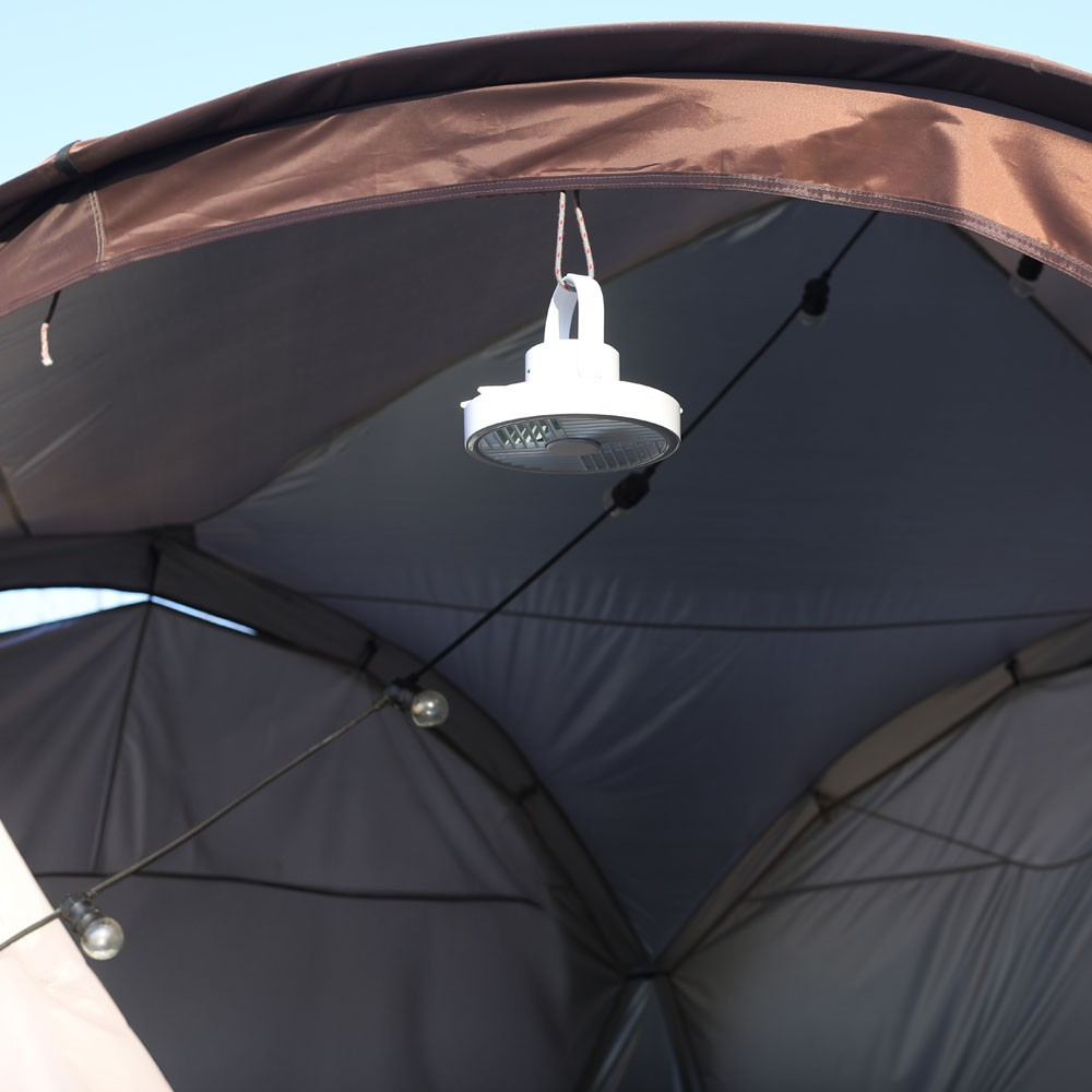Un ventilador blanco con luz cuelga de una tela de tienda marrón.