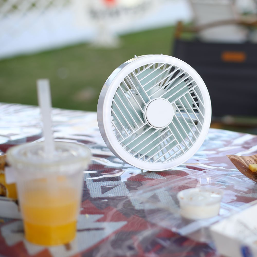 Un pequeño ventilador blanco está sobre una mesa junto a una bebida.
