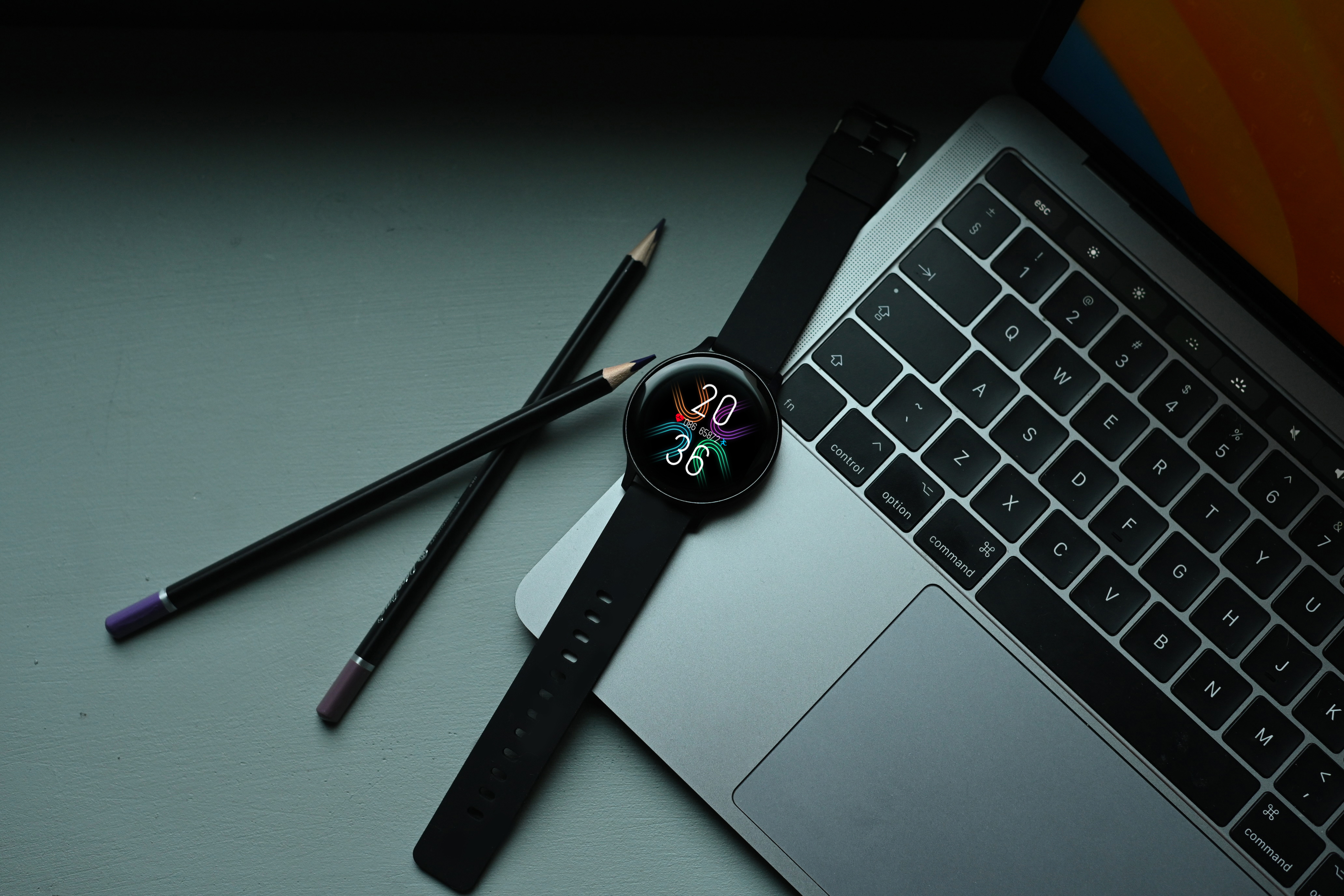 Smartwatch, dwa ołówki i laptop na stole.
