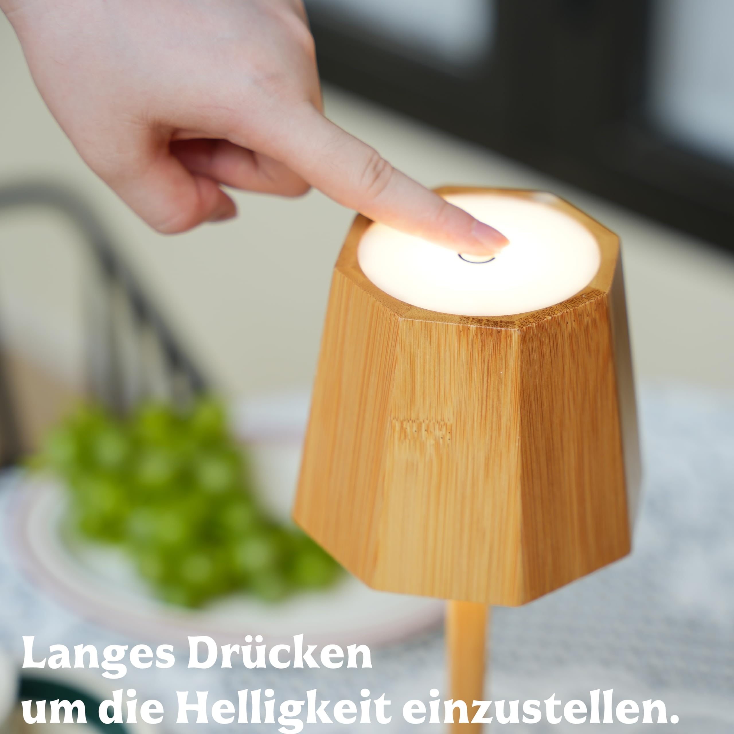 Eine Hand berührt eine leuchtende Lampe aus Holz. Trauben sind im Hintergrund.