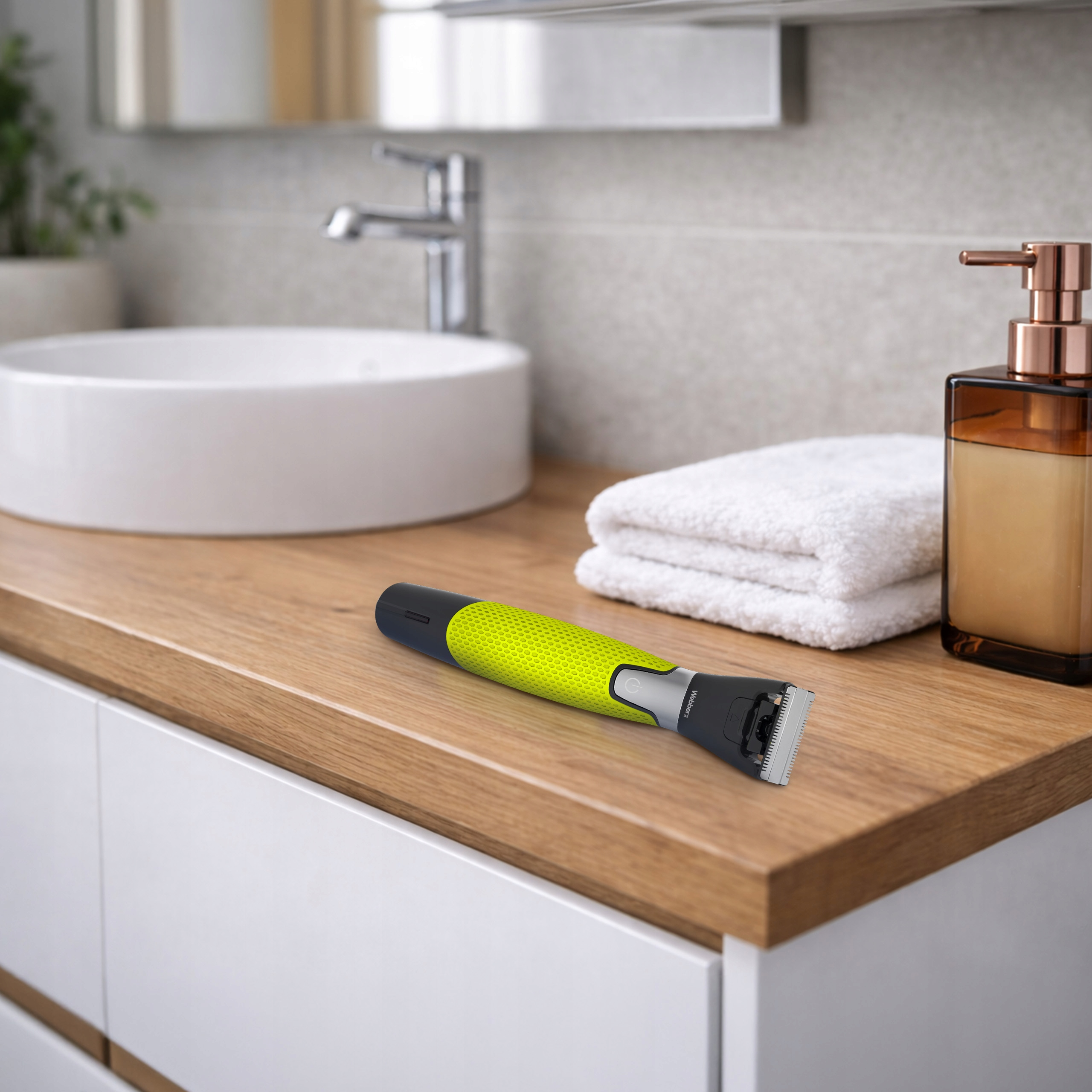 Żółta maszynka do strzyżenia leży na drewnianej powierzchni obok umywalki i ręczników.