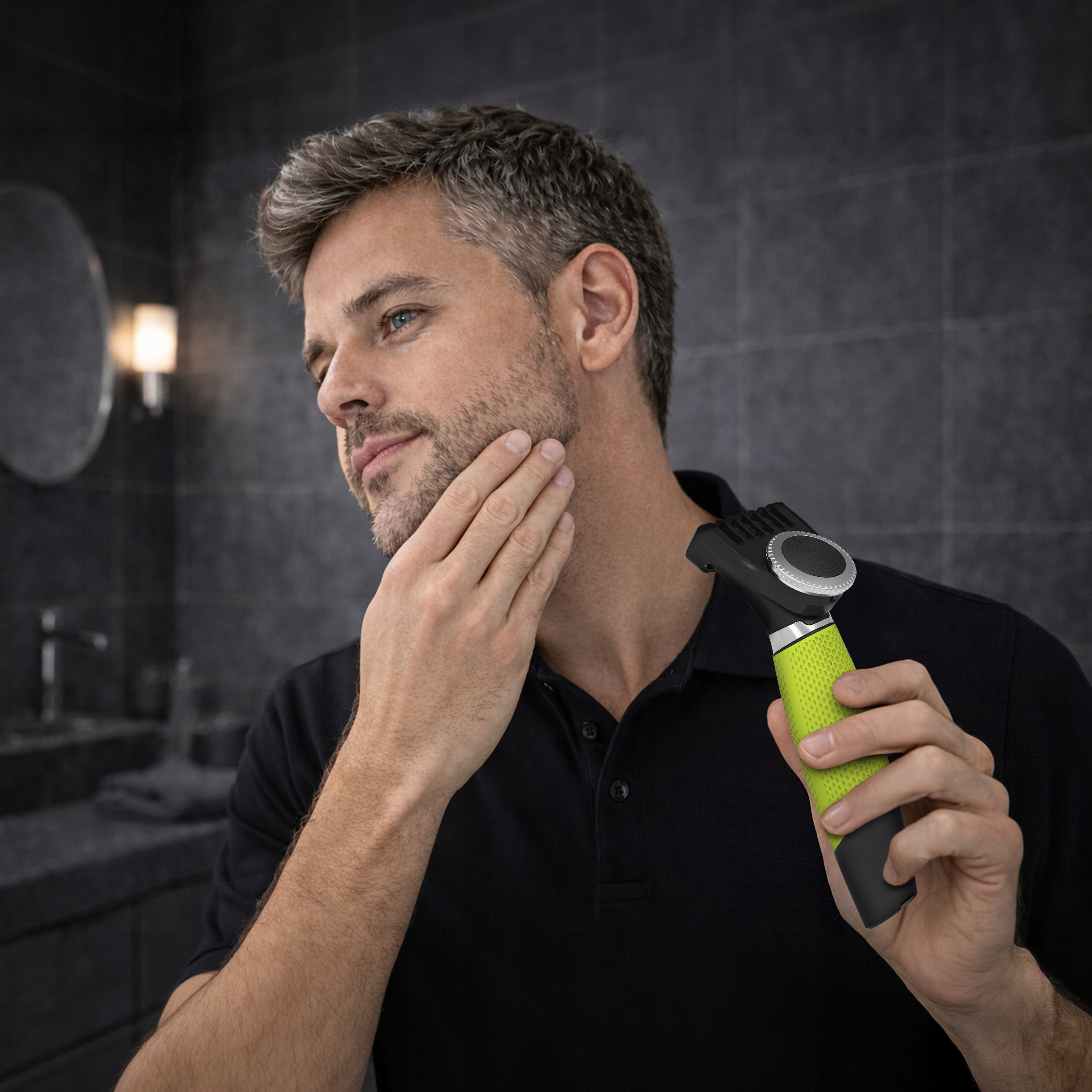 Mężczyzna z siwiejącymi włosami i niebieskimi oczami, trzyma zieloną elektryczną maszynkę, w nowoczesnej łazience.