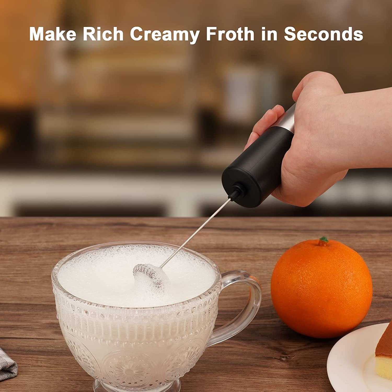 Hand hält Milchaufschäumer in Tasse mit Milch. Orange und Kuchen daneben.
