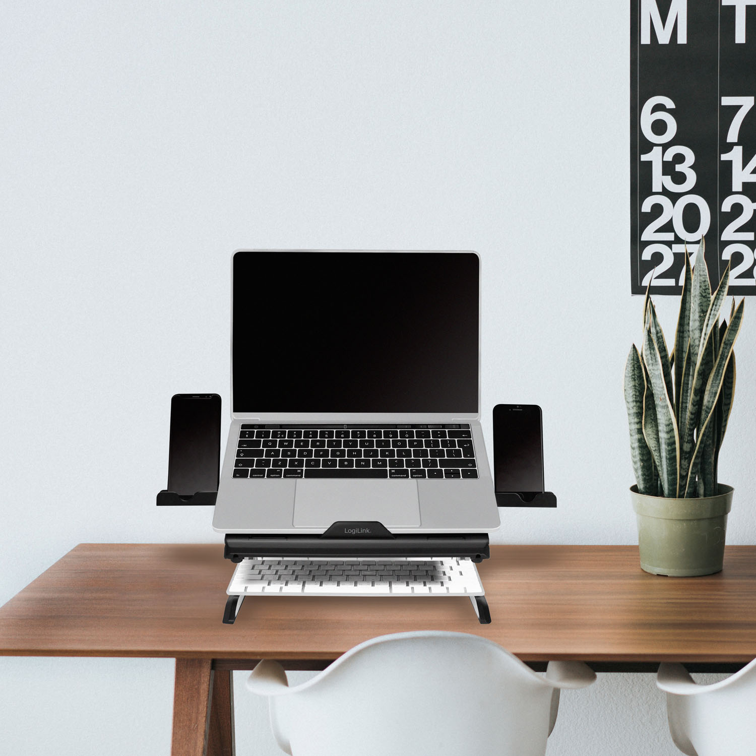 Laptop stoi na podstawce nad klawiaturą. Po bokach dwa telefony.