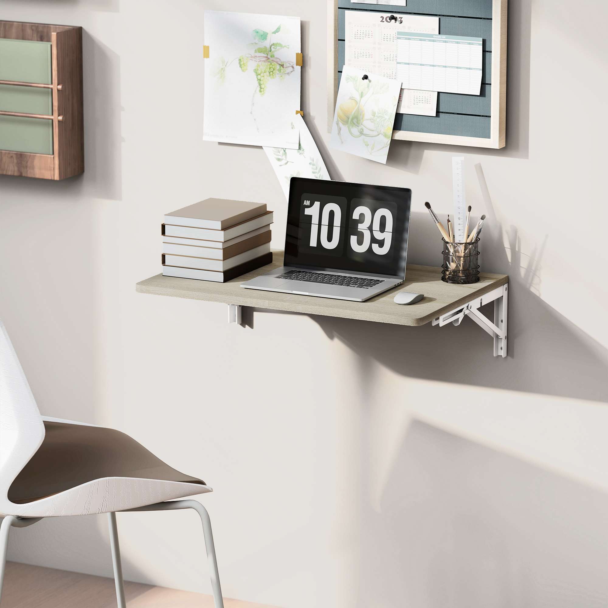 Ein klappbarer Schreibtisch an der Wand mit Laptop, Büchern und Kunstbedarf. Ein Stuhl ist im Vordergrund.