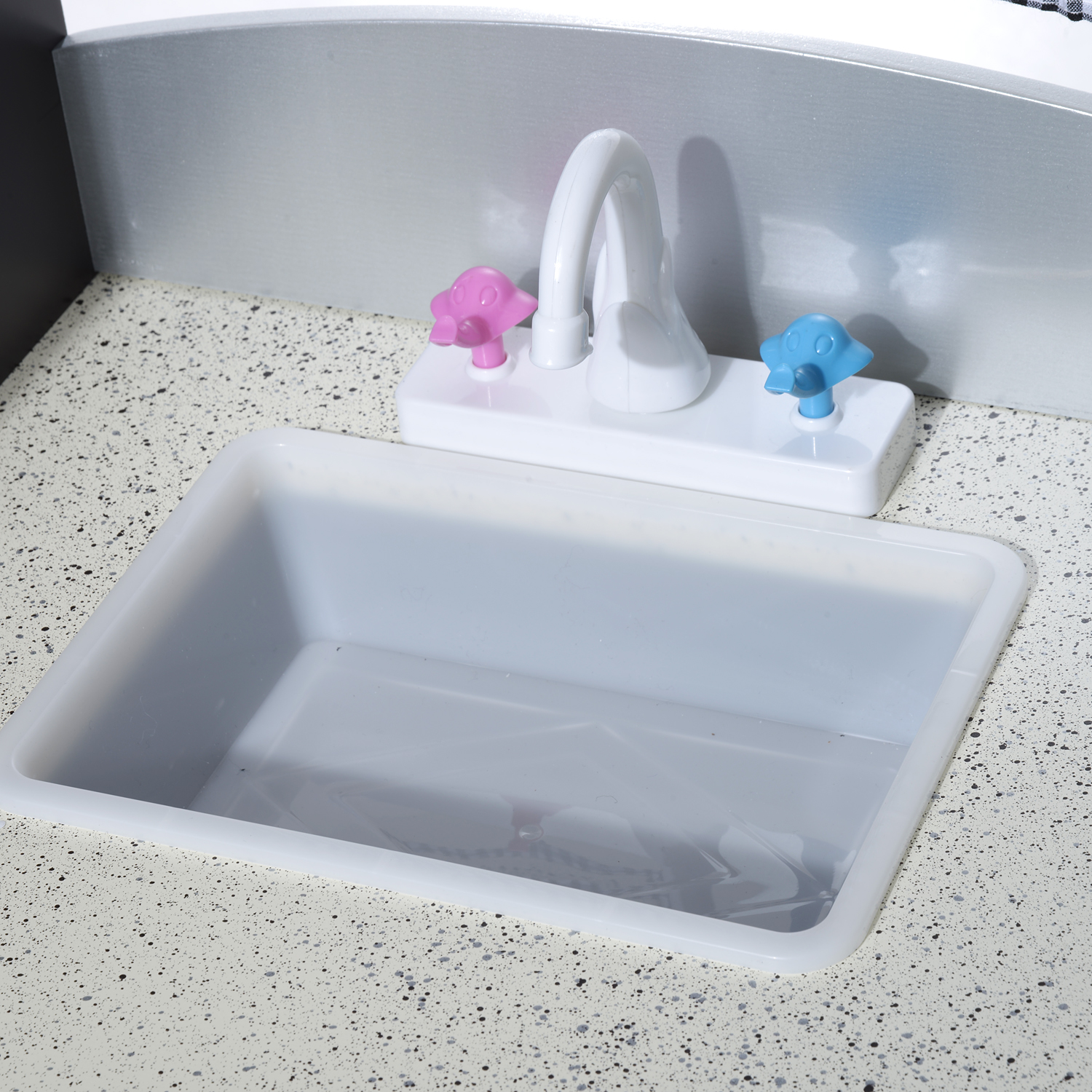 Un lavabo de juguete blanco con grifo y mandos coloridos sobre encimera.