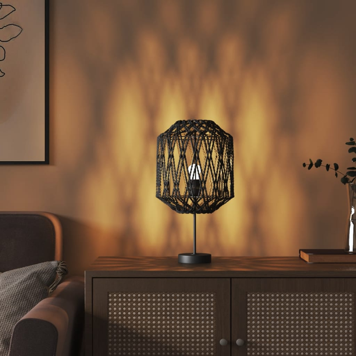 Eine schwarze Tischlampe mit einem geflochtenen Schirm steht auf einem dunklen Schrank.