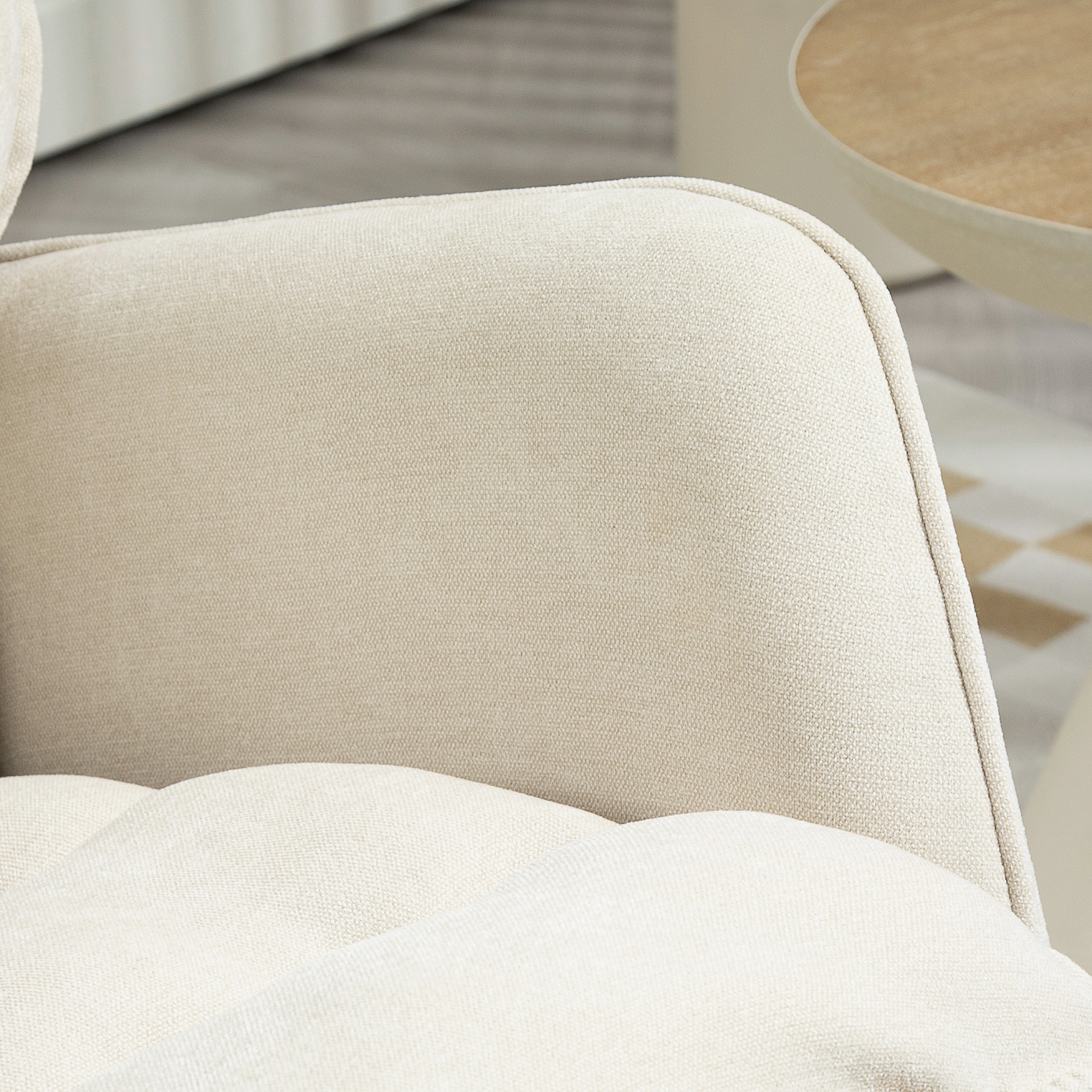 Primer plano de una silla de tela beige con asiento capitoné y parte de una mesa redonda.