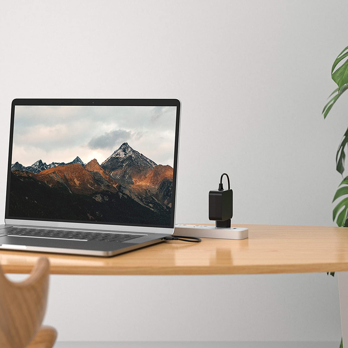 Ein Laptop mit Berglandschaft auf dem Bildschirm steht auf einem Holztisch neben einer Steckdosenleiste.