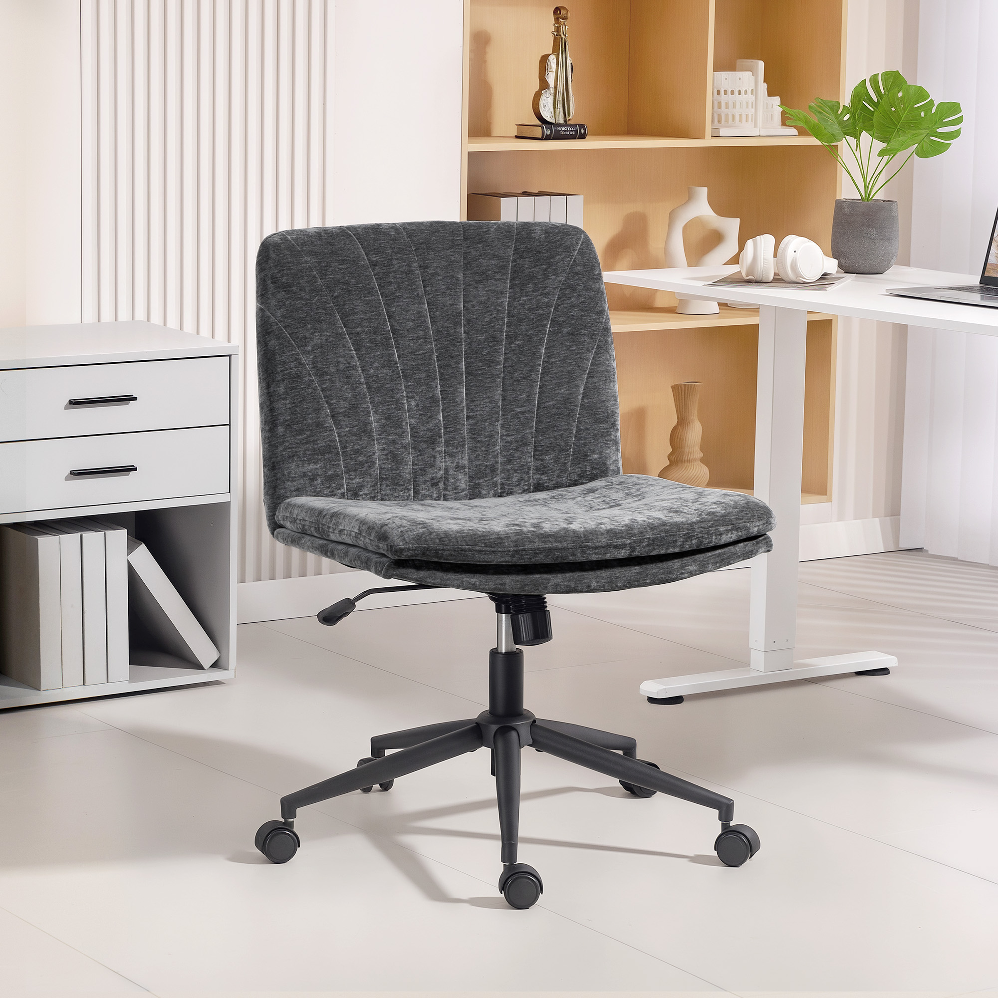 Una silla de oficina gris con ruedas se sienta frente a un gabinete blanco y una estantería.