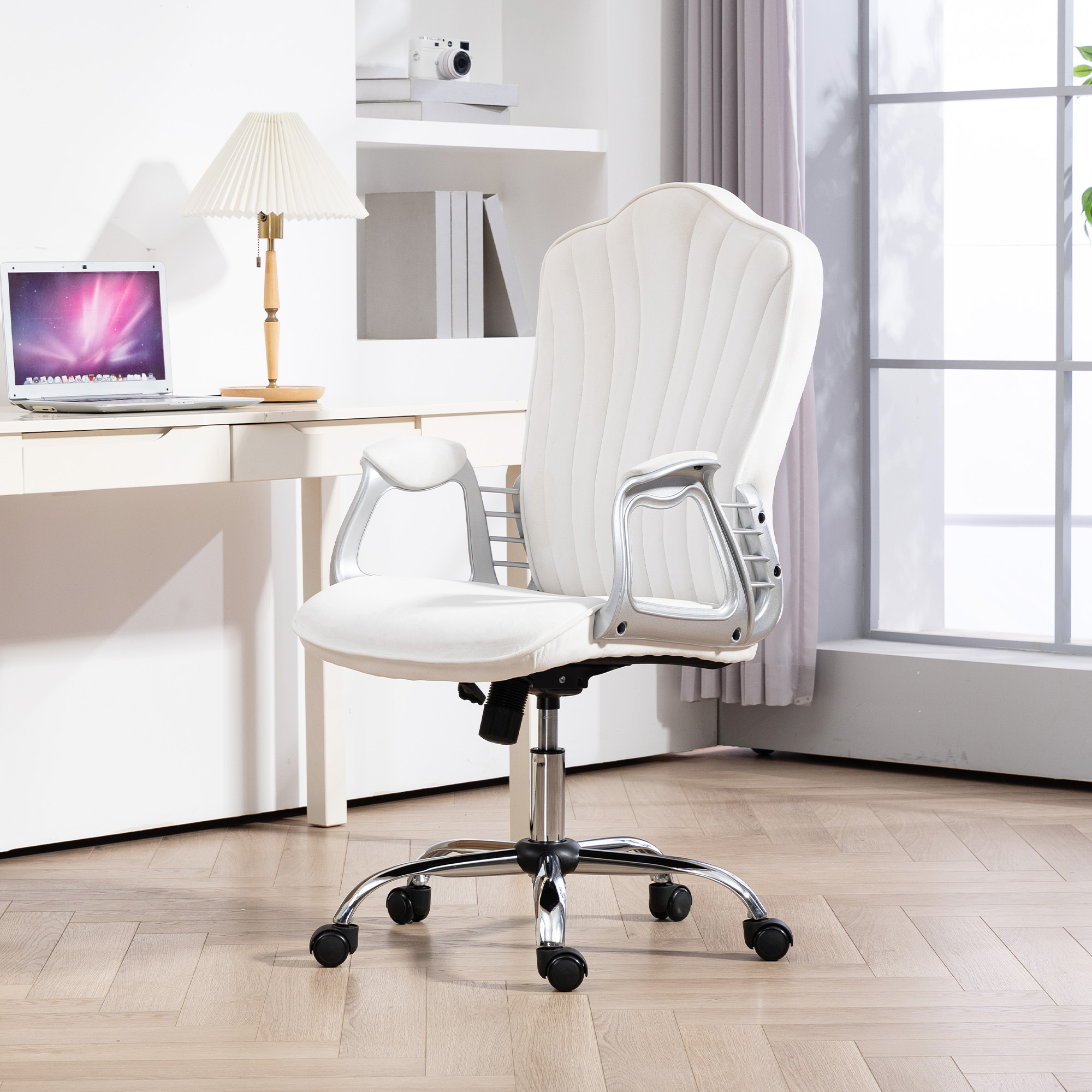 Una silla de oficina blanca con detalles plateados junto a un escritorio con portátil y lámpara.