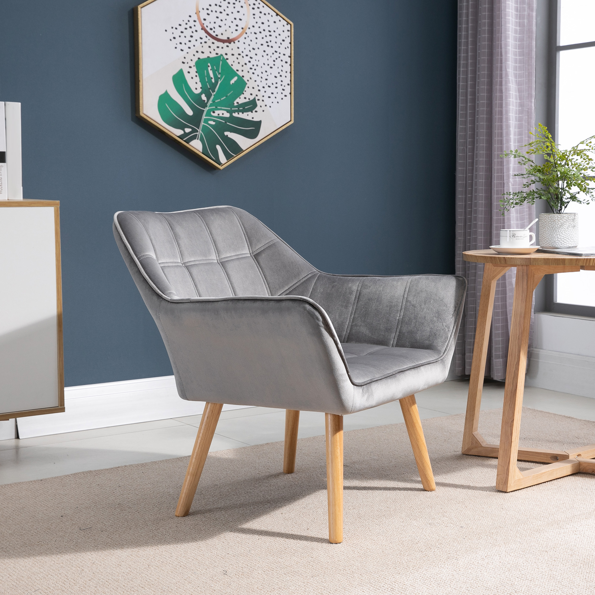 Un sillón gris con patas de madera se sienta sobre una alfombra junto a una mesa de madera.