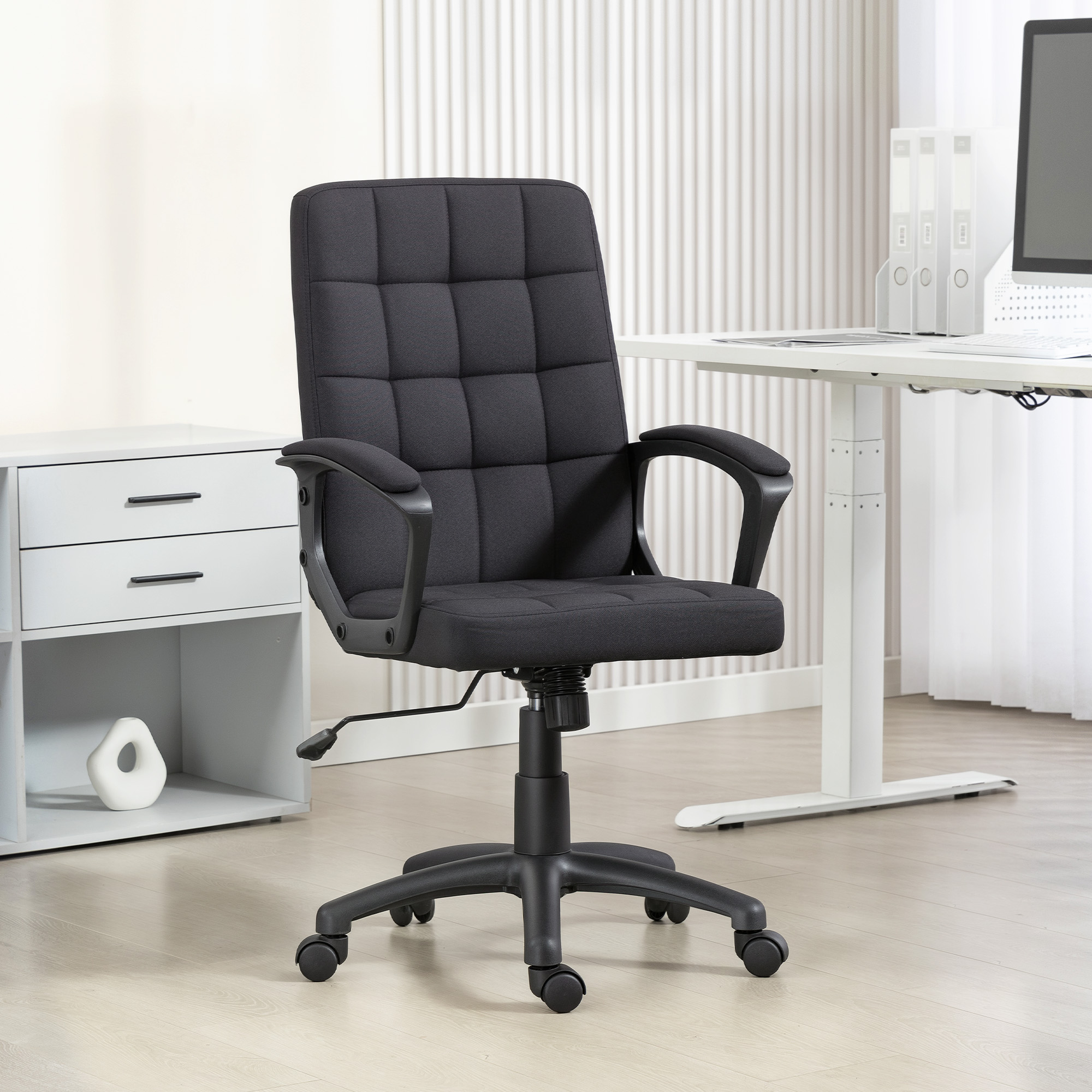 Silla de oficina tapizada negra con ruedas frente a un escritorio y estante blancos.