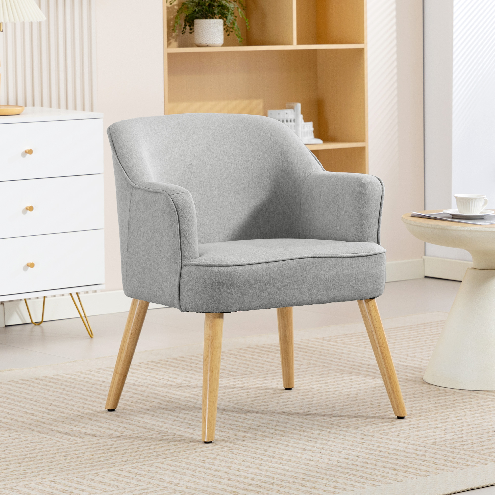 Un sillón gris con patas de madera se sienta sobre una alfombra junto a una mesa auxiliar blanca.