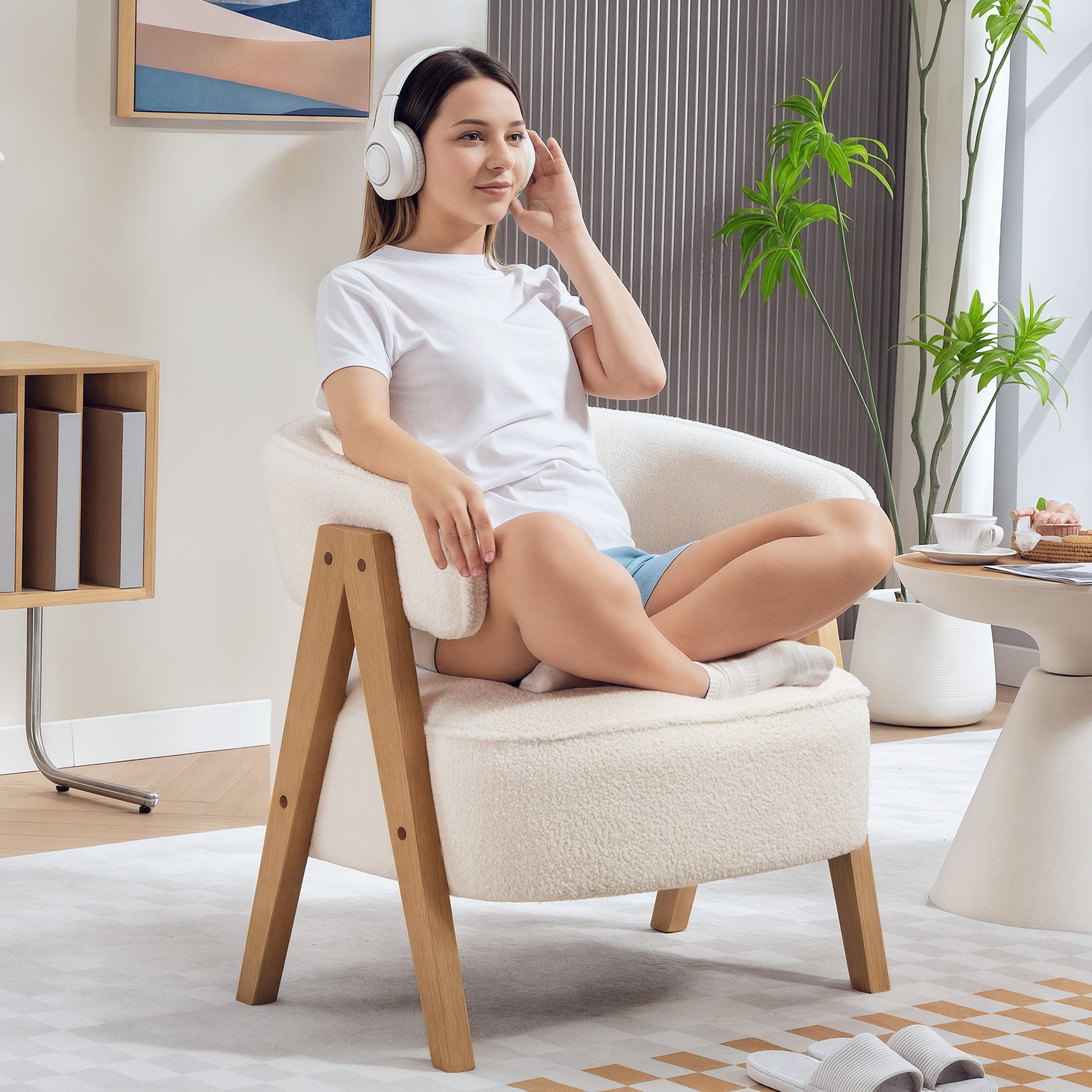 Mujer joven con auriculares sentada en posición de loto en sillón, con planta y mesa al fondo.