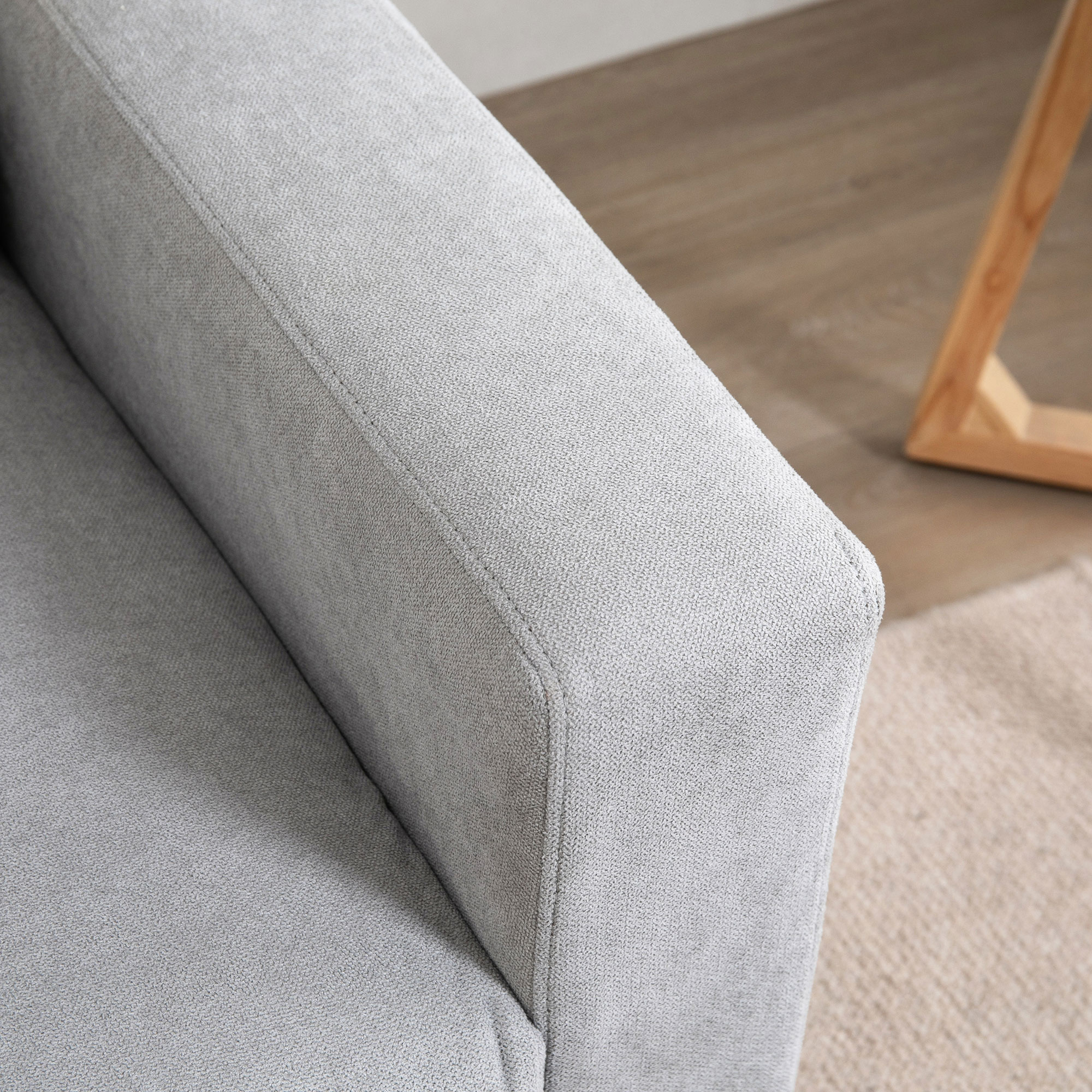 Reposabrazos de sofá de tela gris con detalles de costura y suelo de madera.
