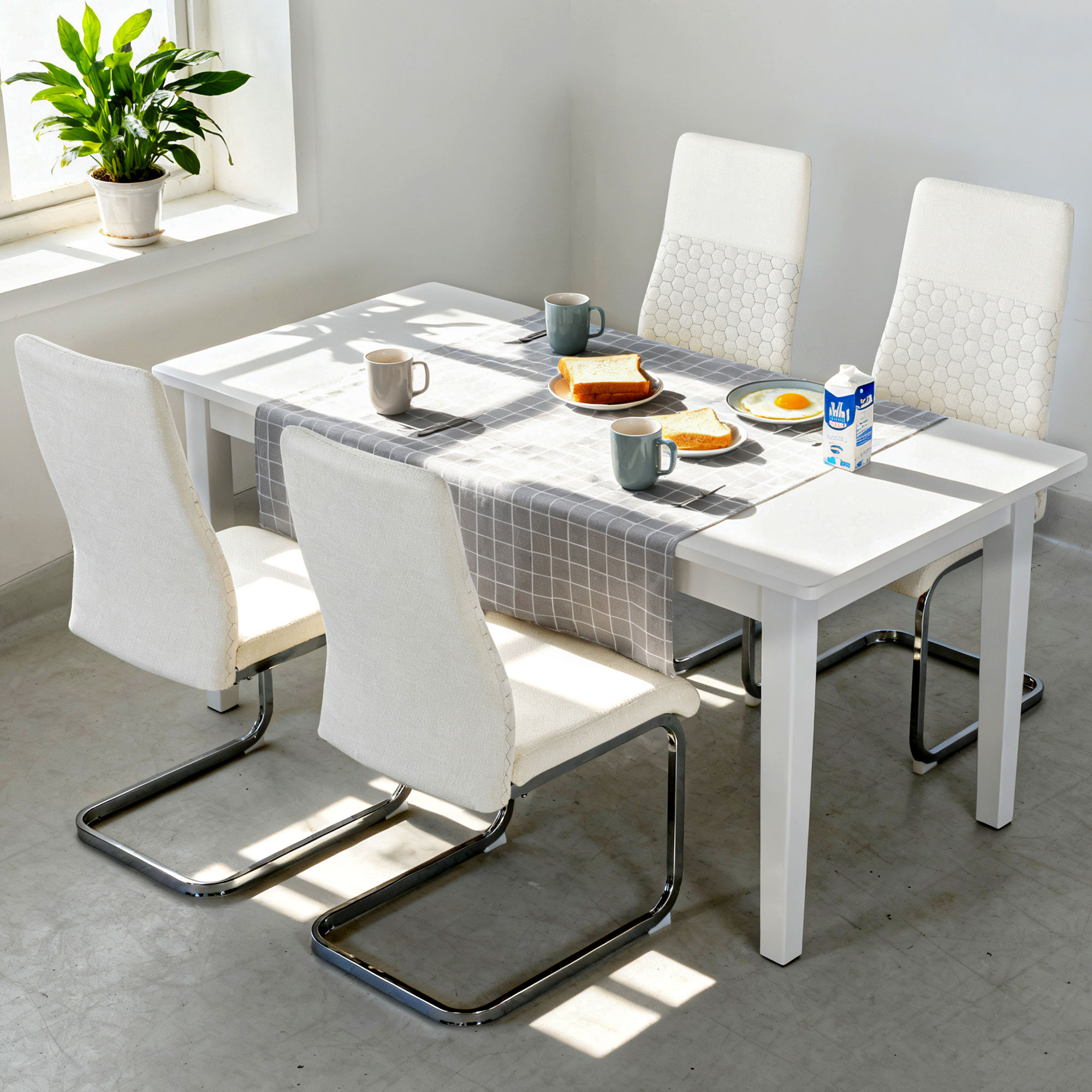 Una mesa blanca puesta para el desayuno con cuatro sillas, una planta y luz solar.