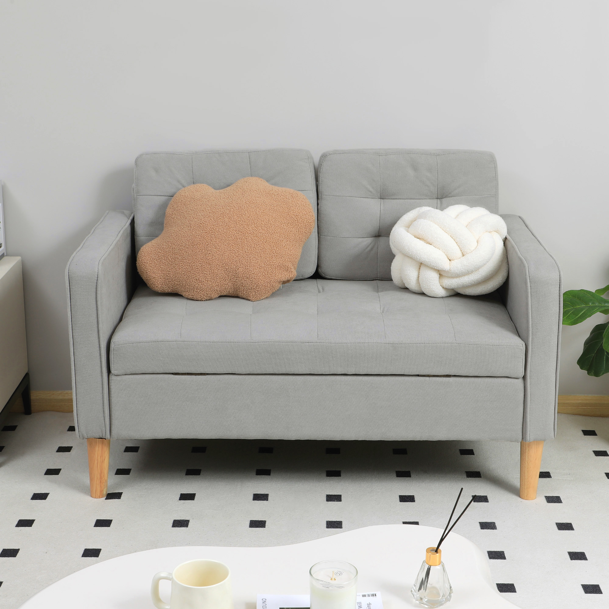 Un sofá gris con dos cojines decorativos: uno en forma de nube y color canela, el otro blanco anudado.